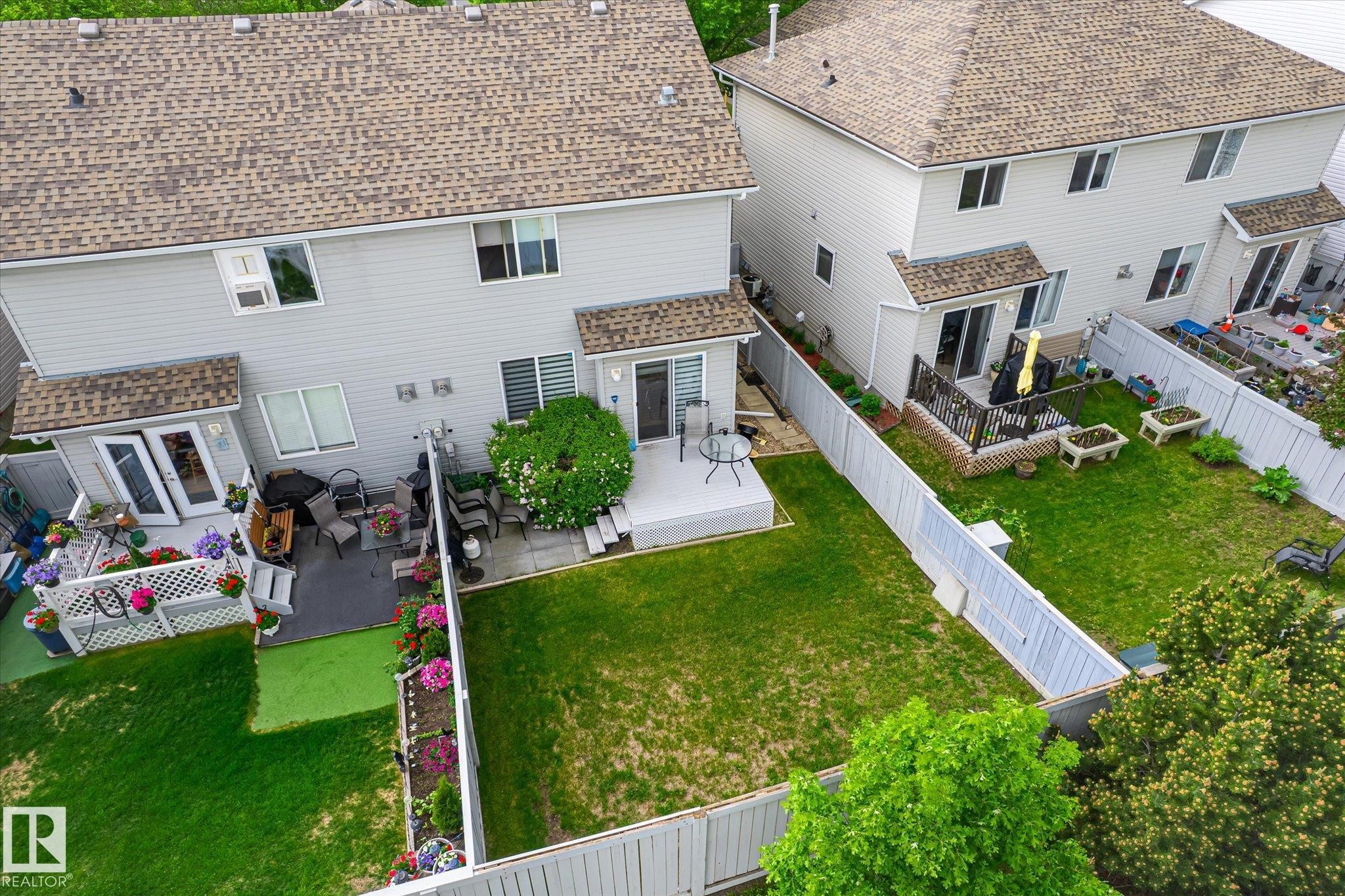 Expansive backyard featuring a manicured lawn, a raised wooden deck, a second ground-level patio, and privacy fencing - #37 4020 21 St Nw, Edmonton, AB - Outdoor With Exterior