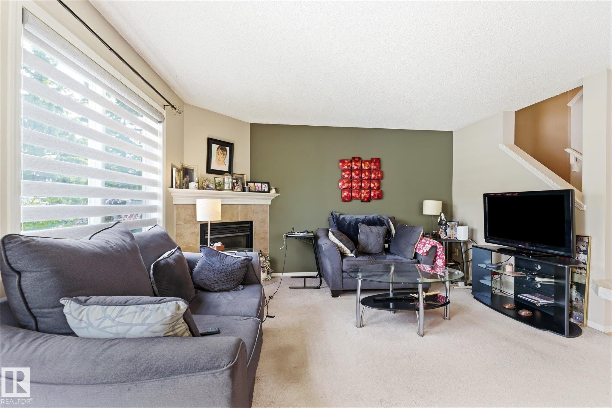 Living area featuring a textured accent wall, light-colored carpeting, and a fireplace with a stone surround and mantel - #37 4020 21 St Nw, Edmonton, AB - Indoor Photo Showing Living Room With Fireplace