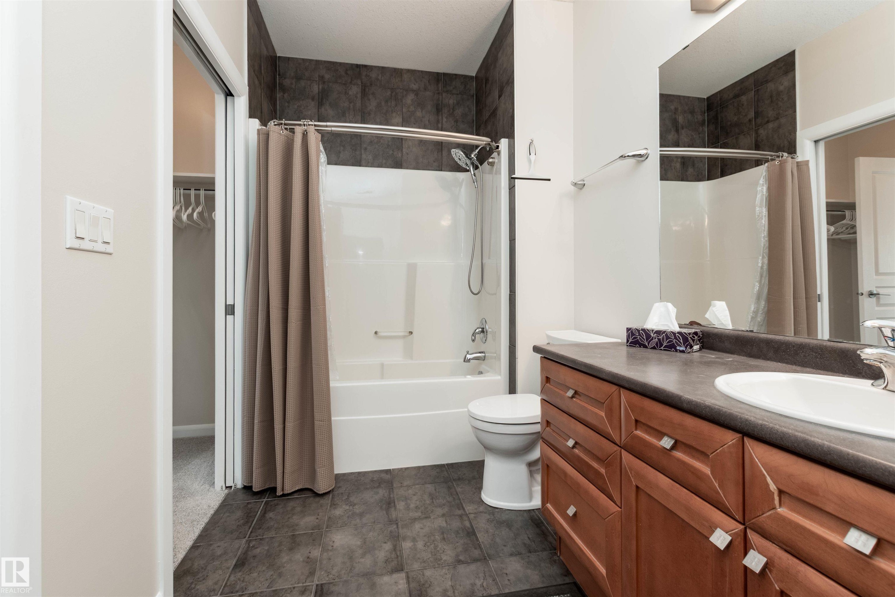 Bathroom featuring a wood-finish vanity with an integrated sink, dark countertop, and large mirror - 439 300 Palisades Way, Sherwood Park, AB - Indoor Photo Showing Bathroom