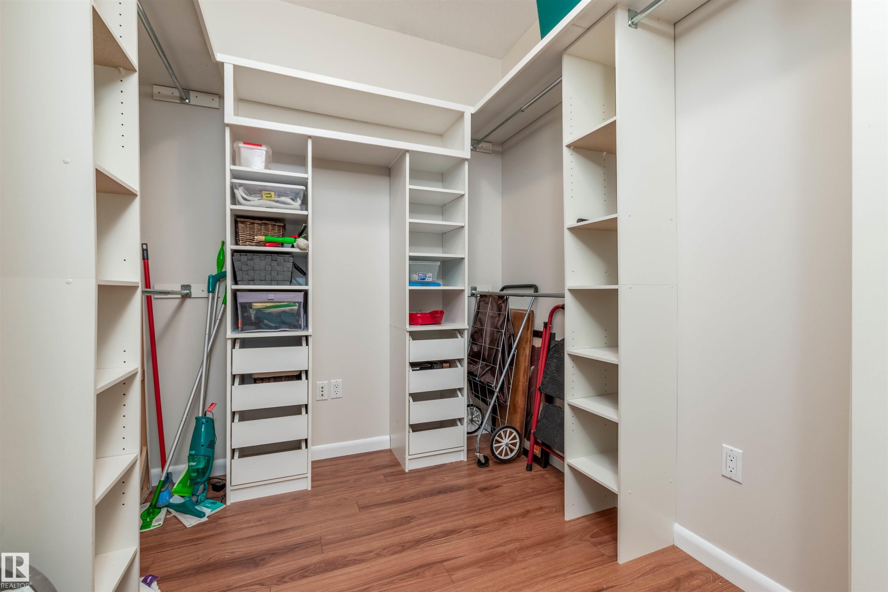 Walk-in closet featuring custom white shelving, built-in drawer units, multiple hanging rods, and wood-finish flooring - 439 300 Palisades Way, Sherwood Park, AB - Indoor Photo Showing Other Room