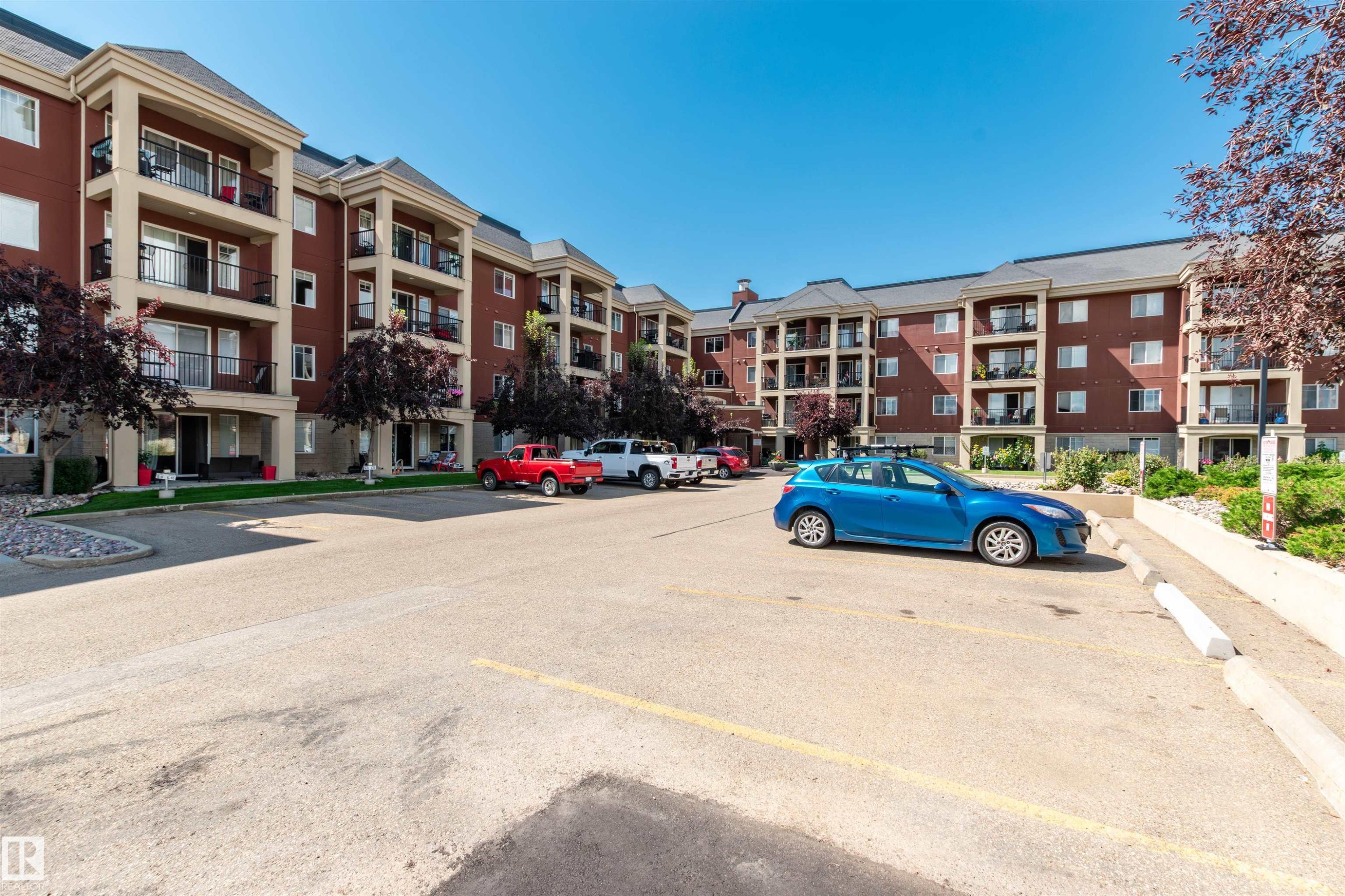 Multi-story building featuring brick and stucco exterior, individual balconies with black railings, and mature landscaping - 439 300 Palisades Way, Sherwood Park, AB - Outdoor With Balcony With Facade