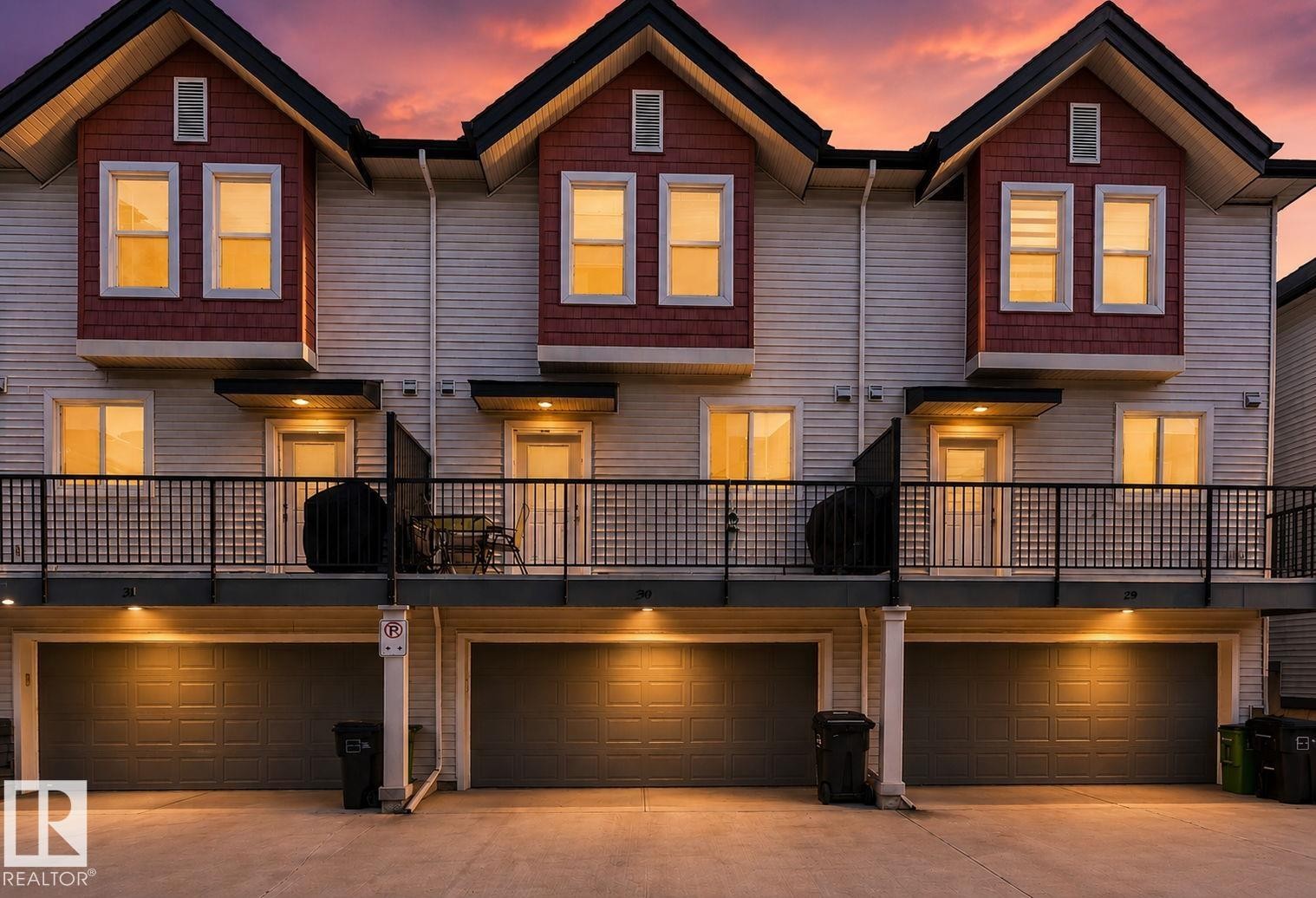 Multi-level townhouse exterior featuring light-toned horizontal siding, red shake accents, and dark pitched roofs - 30 6075 Schonsee Way, Edmonton, AB
