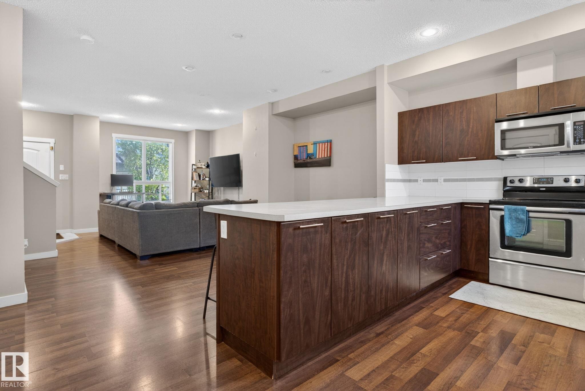 Modern kitchen featuring dark wood cabinetry, white countertops, stainless steel appliances, and a white subway tile backsplash - 30 6075 Schonsee Way, Edmonton, AB