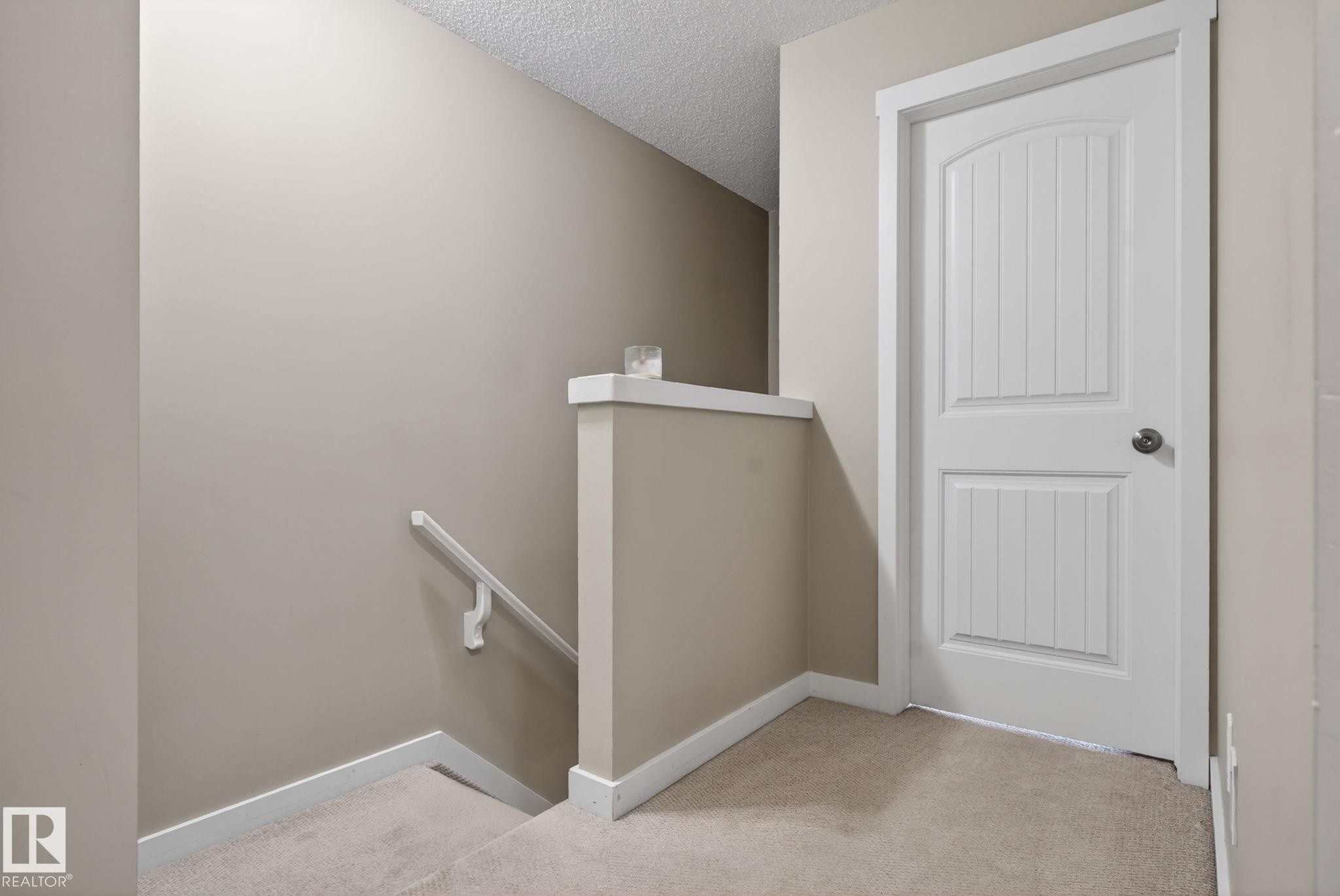 Carpeted landing featuring a white paneled door with a brushed nickel knob, neutral wall paint, and white trim - 30 6075 Schonsee Way, Edmonton, AB