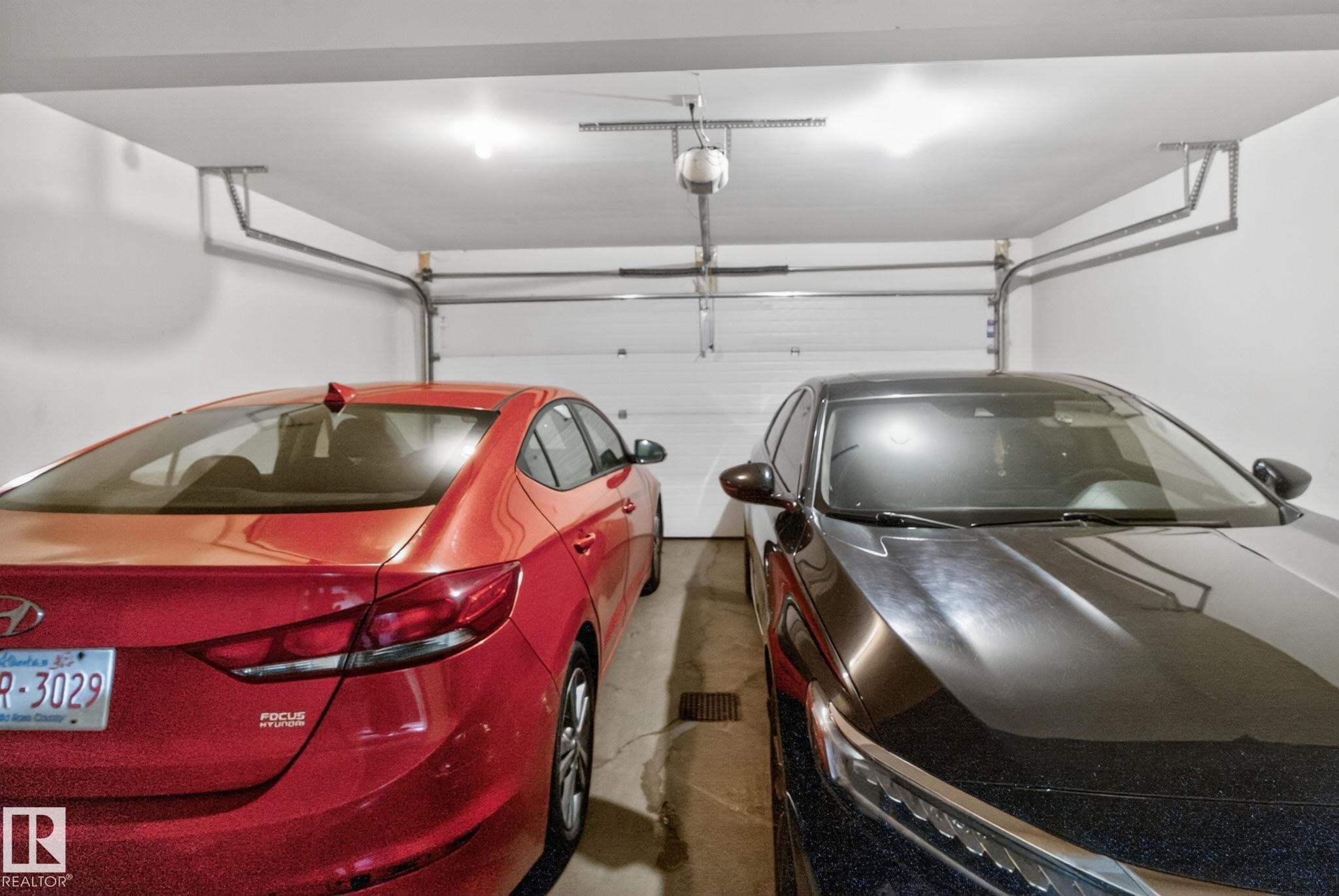 Two-car garage featuring white painted walls and ceiling, two overhead light fixtures, and a white paneled garage door - 30 6075 Schonsee Way, Edmonton, AB