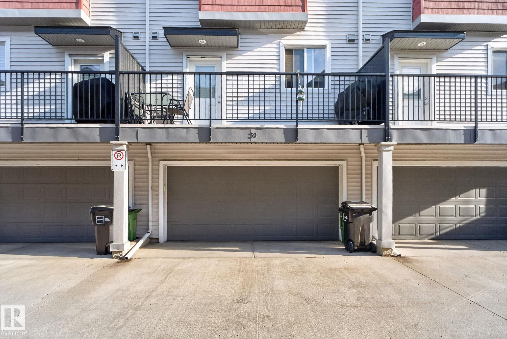 Exterior featuring multiple attached garages with gray panel doors and a concrete driveway - 30 6075 Schonsee Way, Edmonton, AB