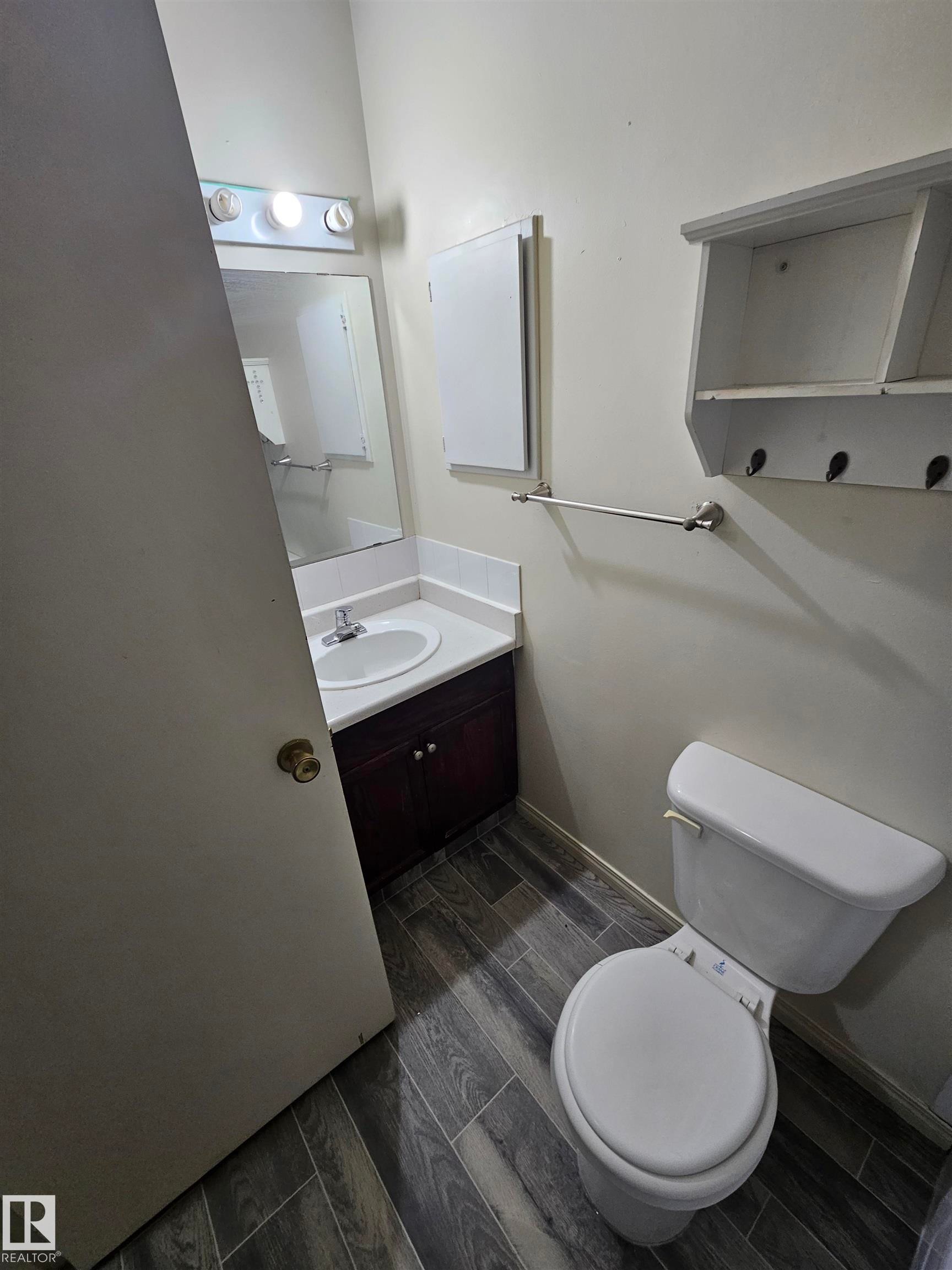 Bathroom featuring wood-finish flooring, a white vanity with an integrated sink, a wall-mounted medicine cabinet, and a white toilet - 401 10615 110 Street, Edmonton, AB