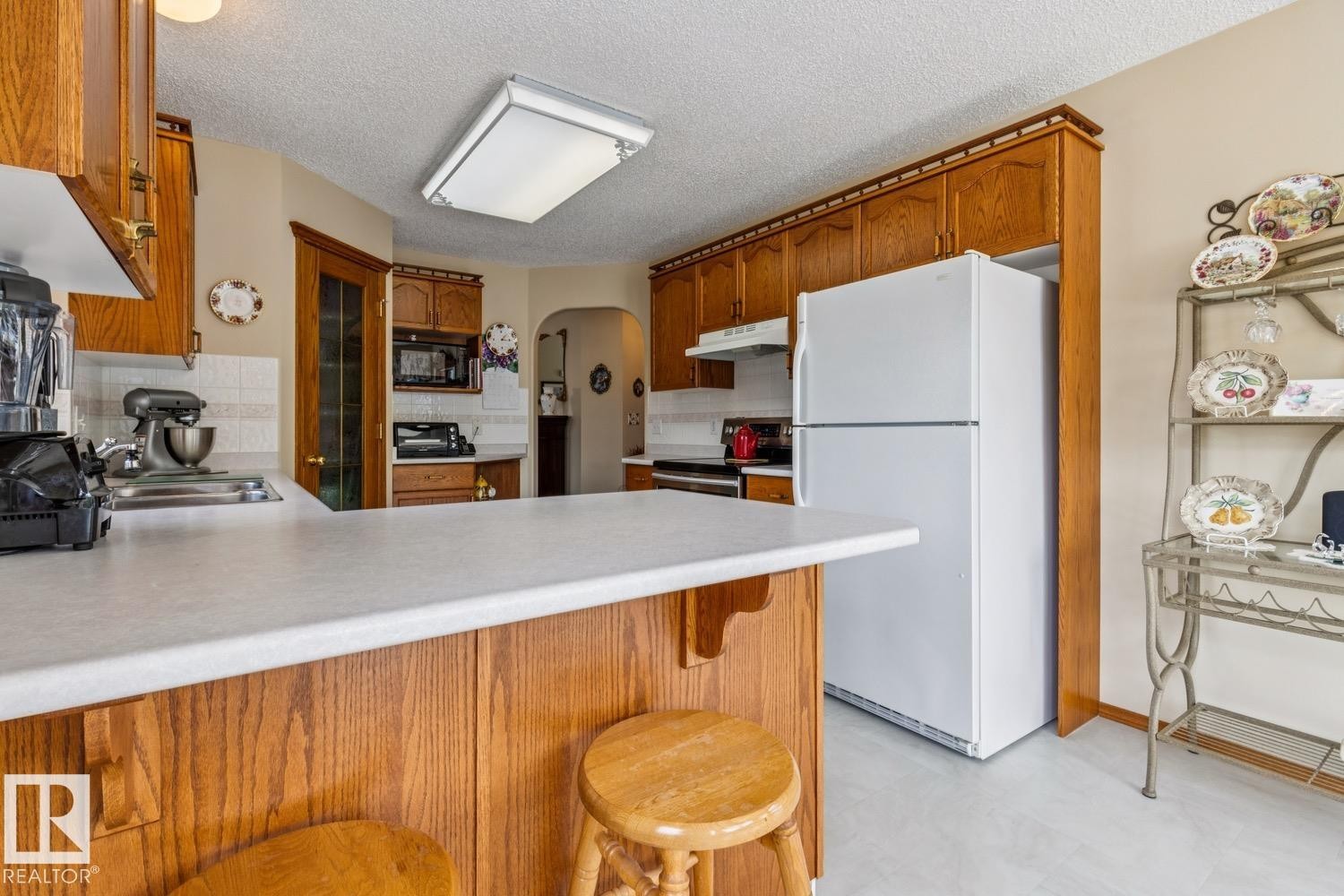 Kitchen featuring wood cabinetry with crown molding, white countertops, space for 2 stools by the counter, tile backsplash, - 5131 152A Avenue, Edmonton, AB