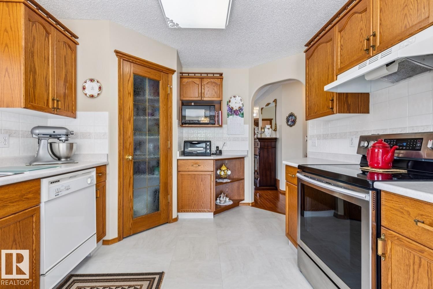 Kitchen featuring wood-finish cabinetry, white countertops, white subway tile backsplash, and light-toned flooring - 5131 152A Avenue, Edmonton, AB