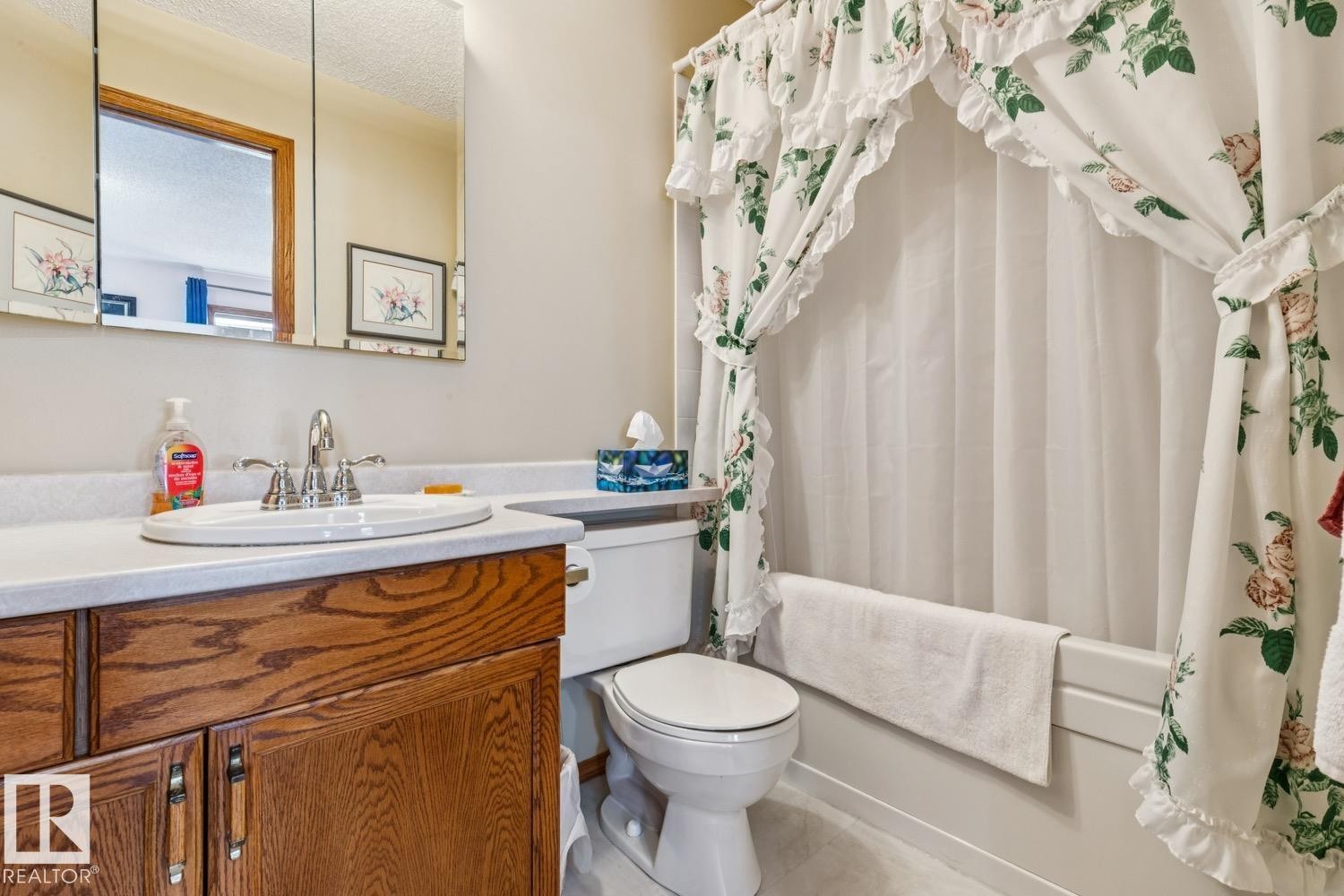 Bathroom featuring a wood-finish vanity with an integrated sink, polished chrome faucet, and a wall-mounted mirrored medicine cabinet - 5131 152A Avenue, Edmonton, AB
