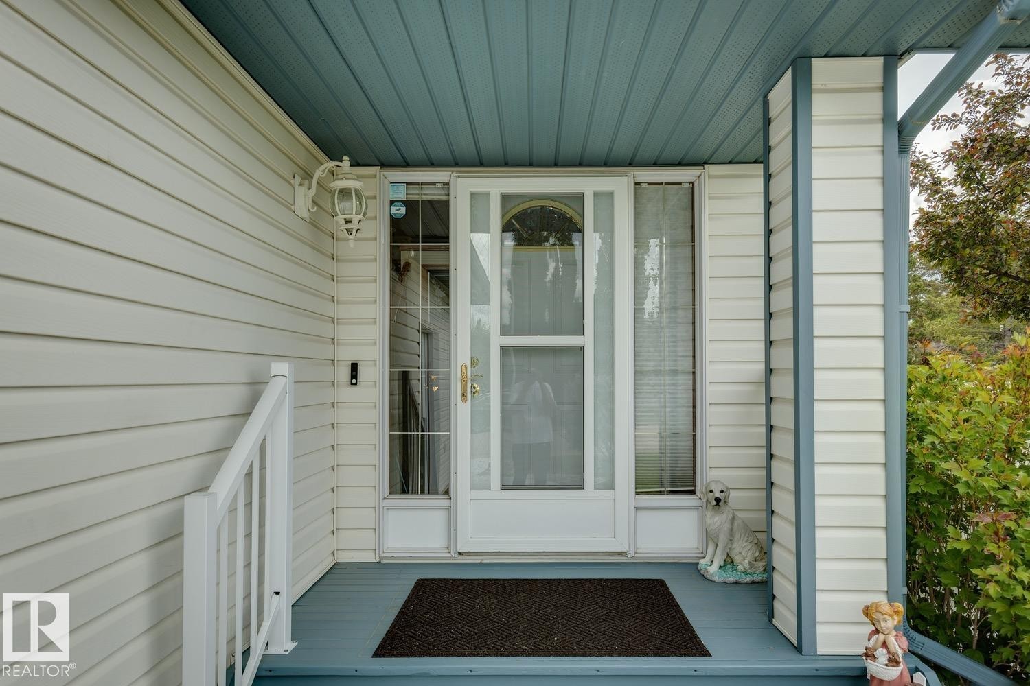 Covered front entry featuring a storm door with glass panels, white siding, and a contrasting blue soffit - 5131 152A Avenue, Edmonton, AB