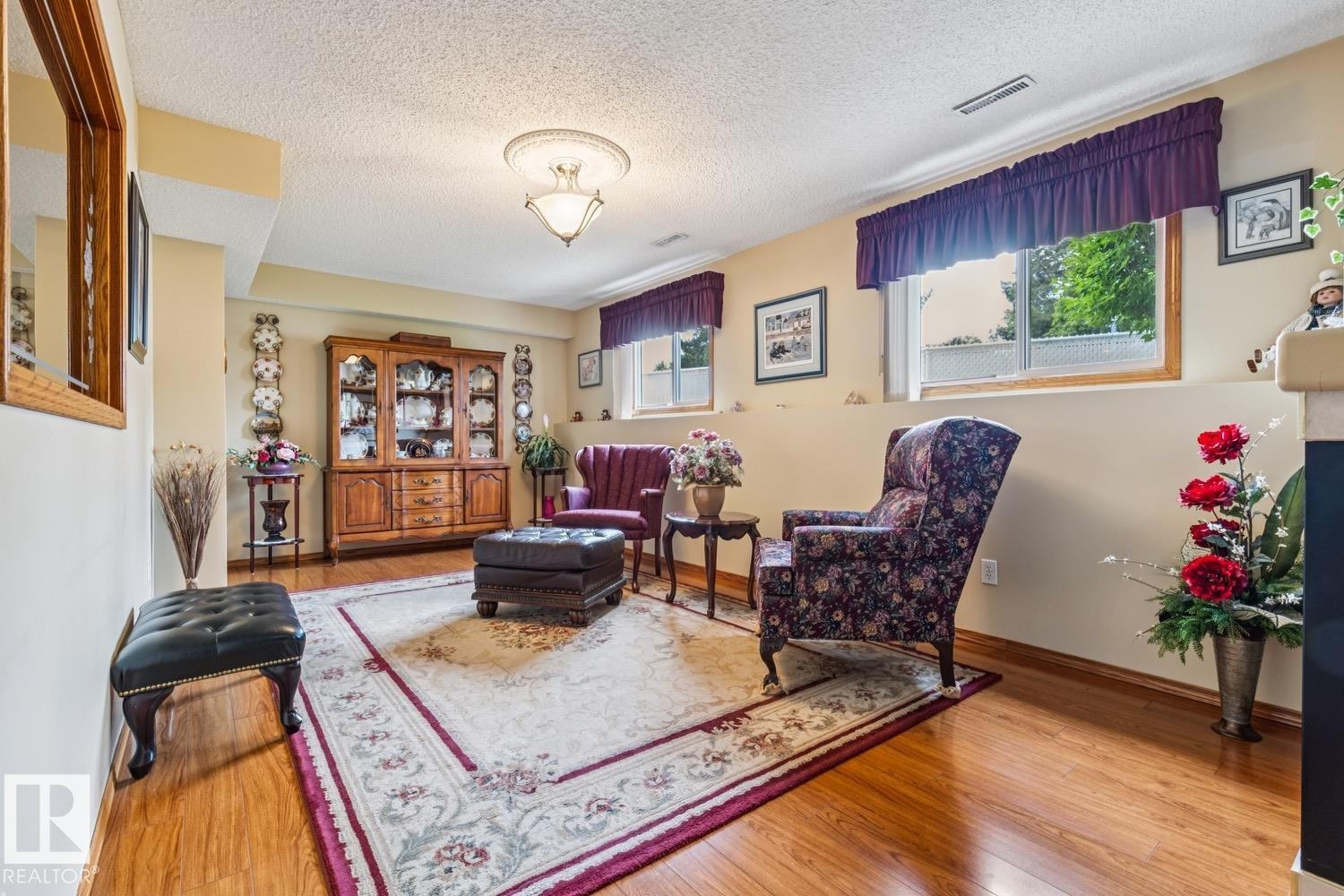 Wood-finish flooring throughout, featuring a built-in display cabinet with glass doors, multiple windows with valances, and a ceiling-mounted light fixture with decorative molding - 5131 152A Avenue, Edmonton, AB