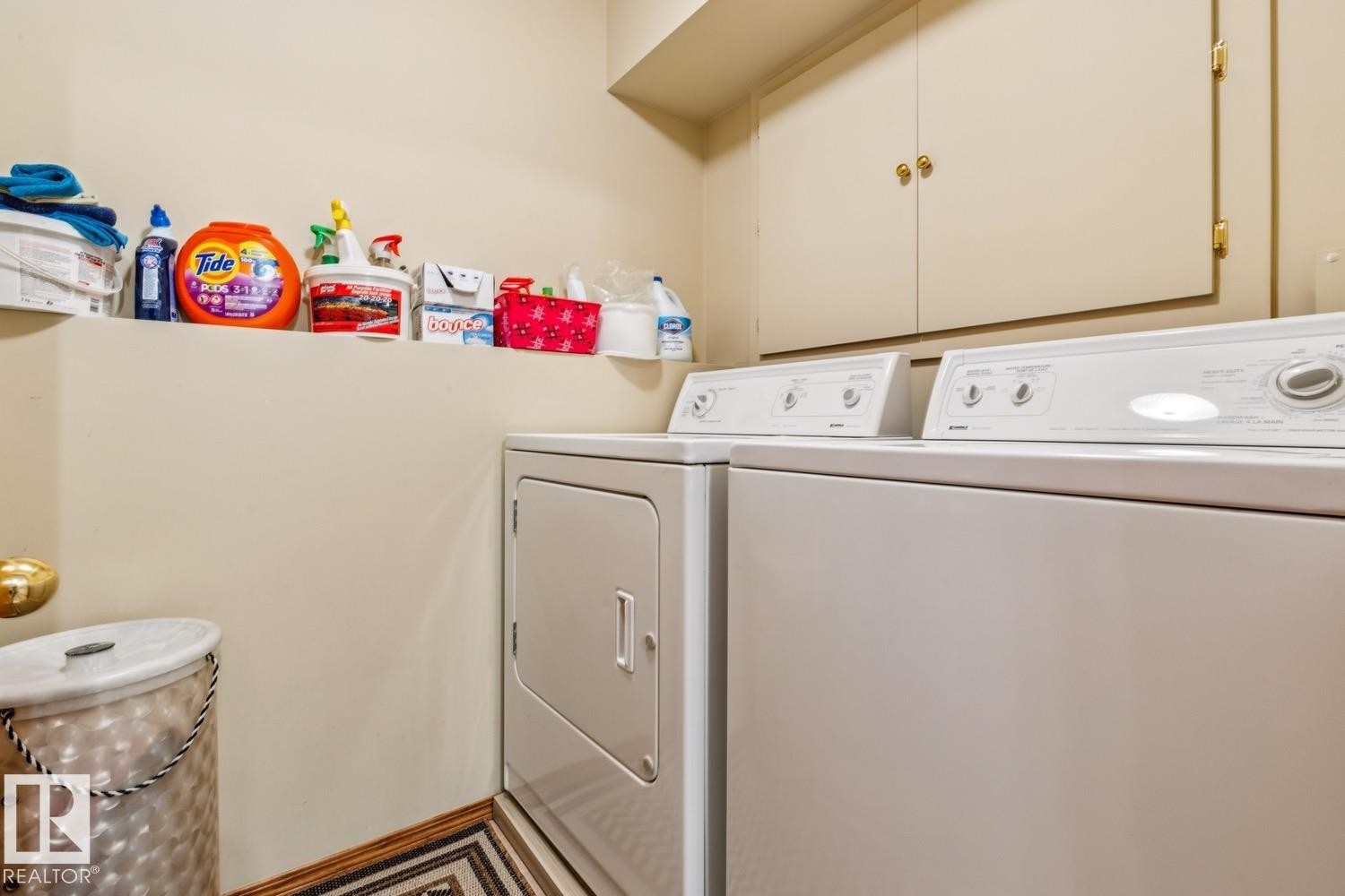 Dedicated laundry area featuring built-in cabinetry, a utility shelf, light-toned walls, and a patterned floor mat - 5131 152A Avenue, Edmonton, AB