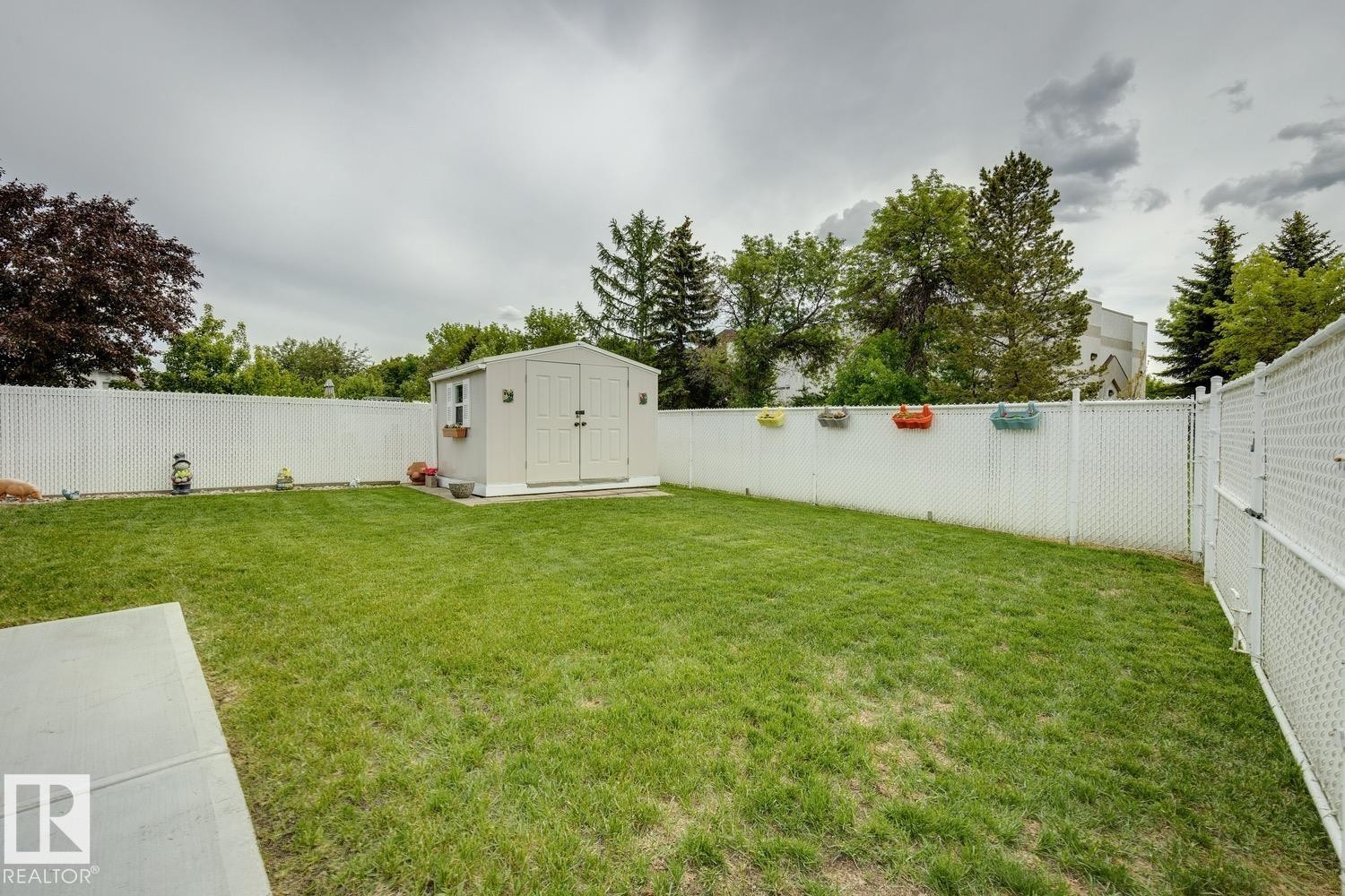Spacious backyard featuring a manicured lawn, a concrete patio, and a white chain-link fence providing enclosure - 5131 152A Avenue, Edmonton, AB
