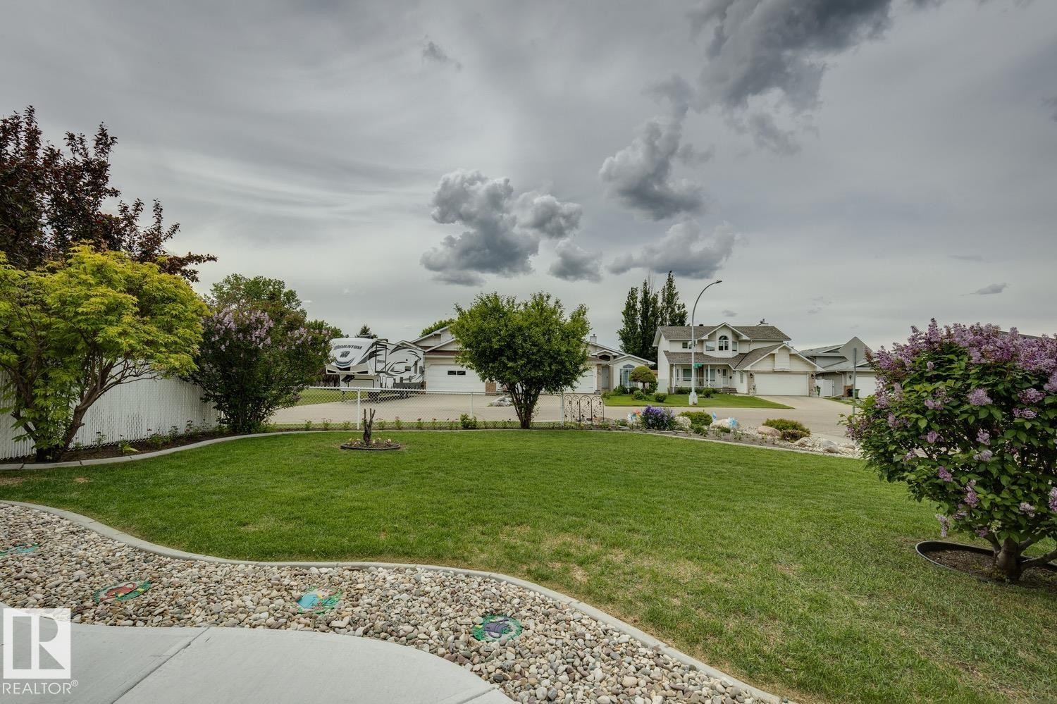 Expansive front yard featuring a manicured lawn, established landscaping, decorative gravel borders, and a concrete pathway - 5131 152A Avenue, Edmonton, AB