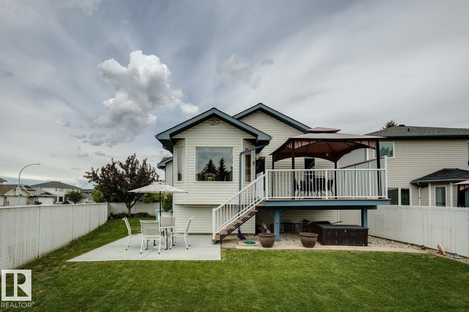 Expansive backyard featuring a manicured lawn, a large elevated deck with white railings, and a ground-level concrete patio - 5131 152A Avenue, Edmonton, AB