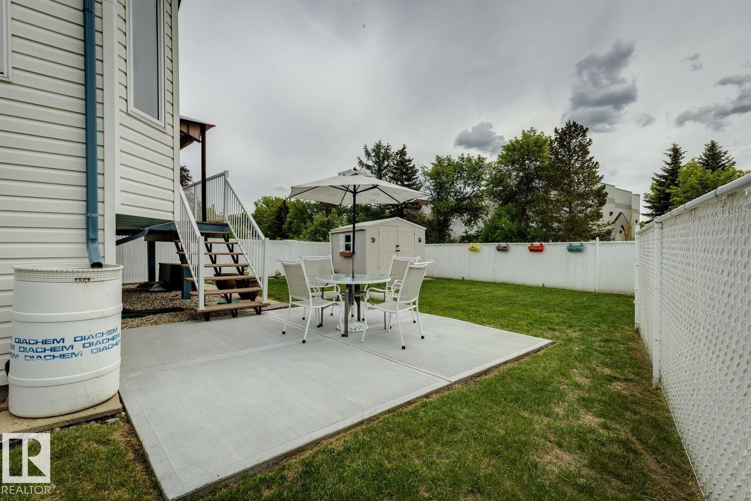 Expansive backyard featuring a concrete patio, green lawn, white privacy fence, and an exterior storage shed - 5131 152A Avenue, Edmonton, AB
