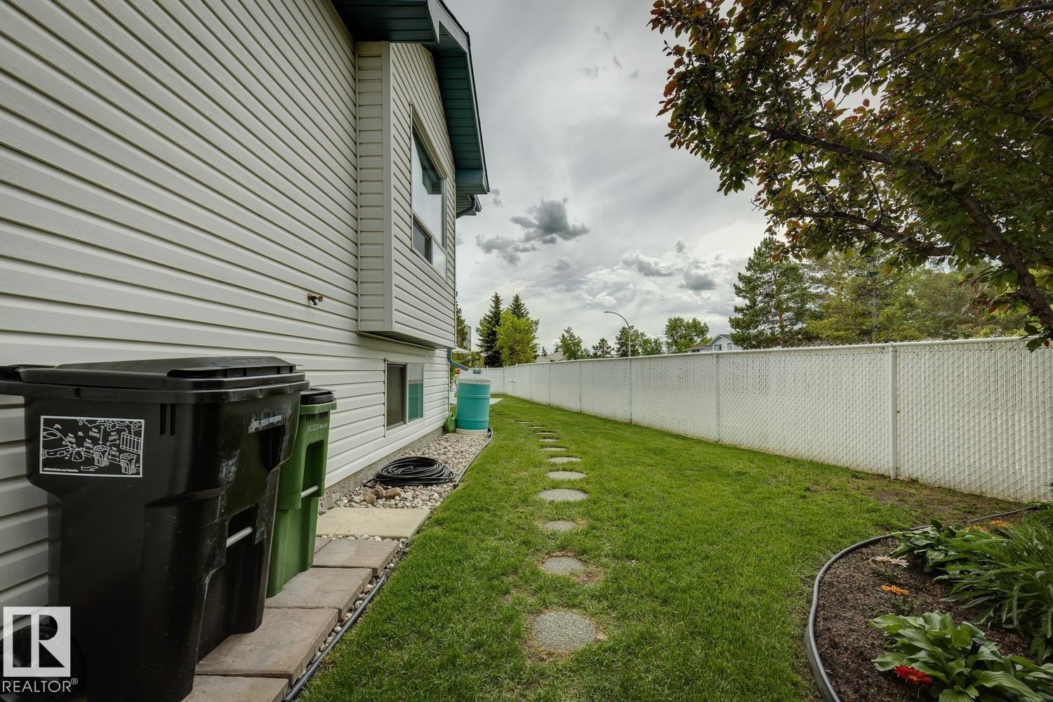 Side yard featuring a stone paver pathway, manicured lawn, and planted garden bed - 5131 152A Avenue, Edmonton, AB