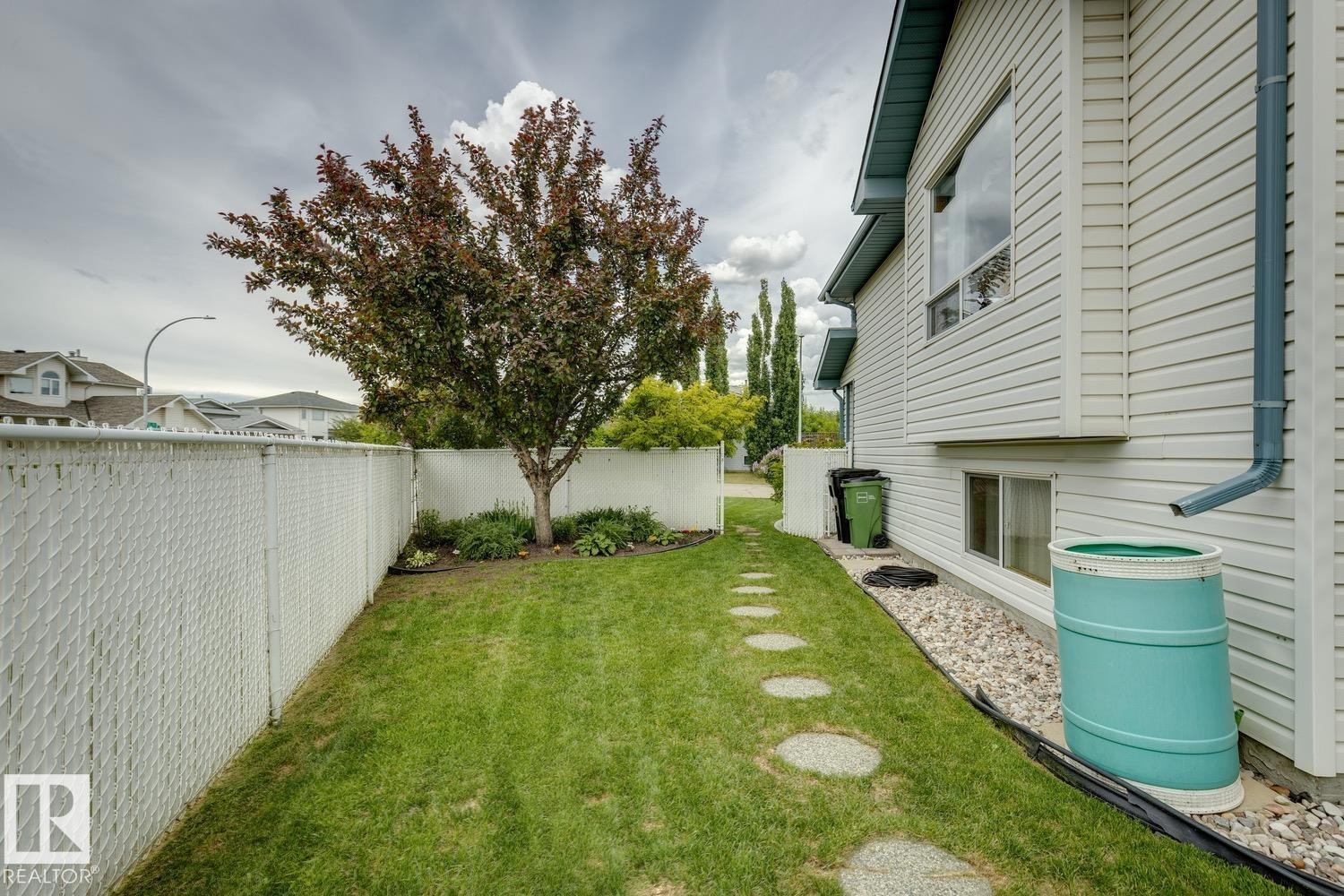 Side yard featuring a manicured lawn, established tree, and a white chain-link fence - 5131 152A Avenue, Edmonton, AB