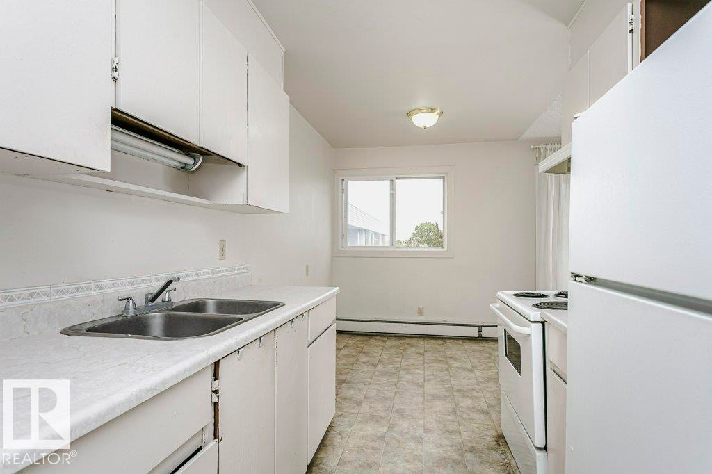 Kitchen featuring white cabinetry, dual basin stainless steel sink, and white appliances - 71 11255 31 Avenue, Edmonton, AB - Indoor Photo Showing Kitchen With Double Sink