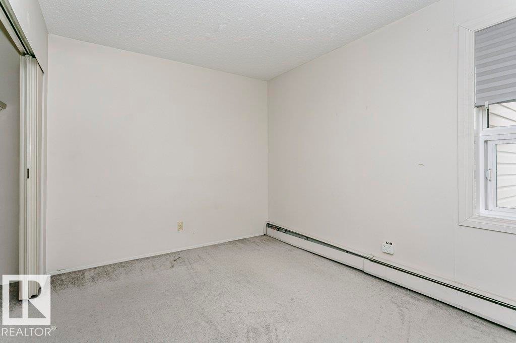 Carpeted room featuring a white window frame, horizontal window blinds, baseboard heating, and a textured ceiling - 71 11255 31 Avenue, Edmonton, AB - Indoor Photo Showing Other Room