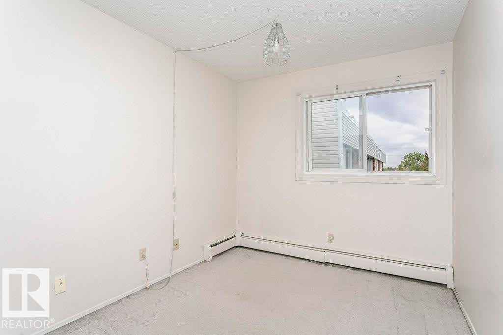 Bright interior room featuring a sliding window, light gray carpet flooring, white walls, and baseboard heating - 71 11255 31 Avenue, Edmonton, AB - Indoor Photo Showing Other Room