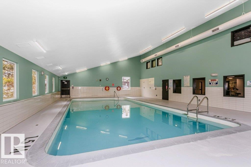 Indoor swimming pool with light blue water and stainless steel entry ladder - 71 11255 31 Avenue, Edmonton, AB - Indoor Photo Showing Other Room With In Ground Pool