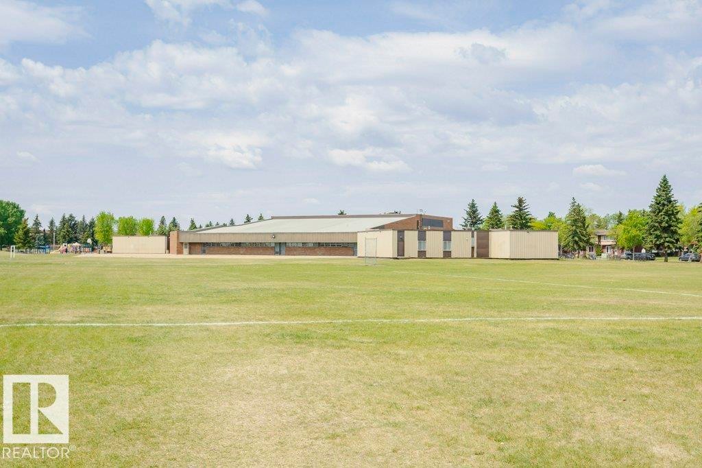 Expansive green field with a distant building featuring a low-sloping roofline, brick facade, and light-colored paneling - 71 11255 31 Avenue, Edmonton, AB - Outdoor
