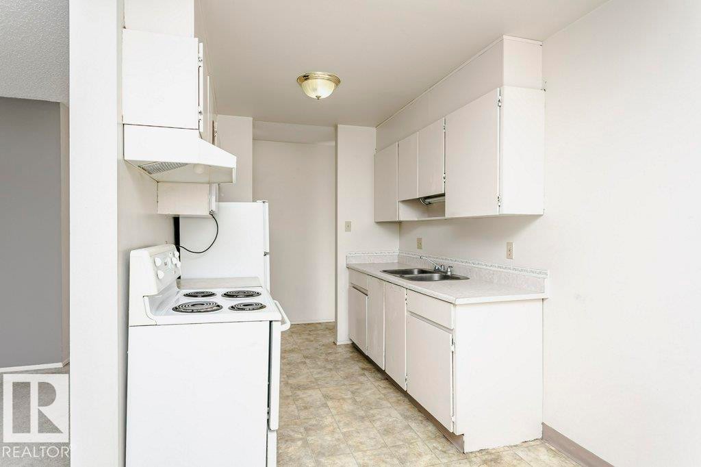 Kitchen featuring white cabinetry, laminate countertops, a double basin stainless steel sink, tile-look vinyl flooring, and a white electric range with range hood - 71 11255 31 Avenue, Edmonton, AB - Indoor Photo Showing Kitchen With Double Sink