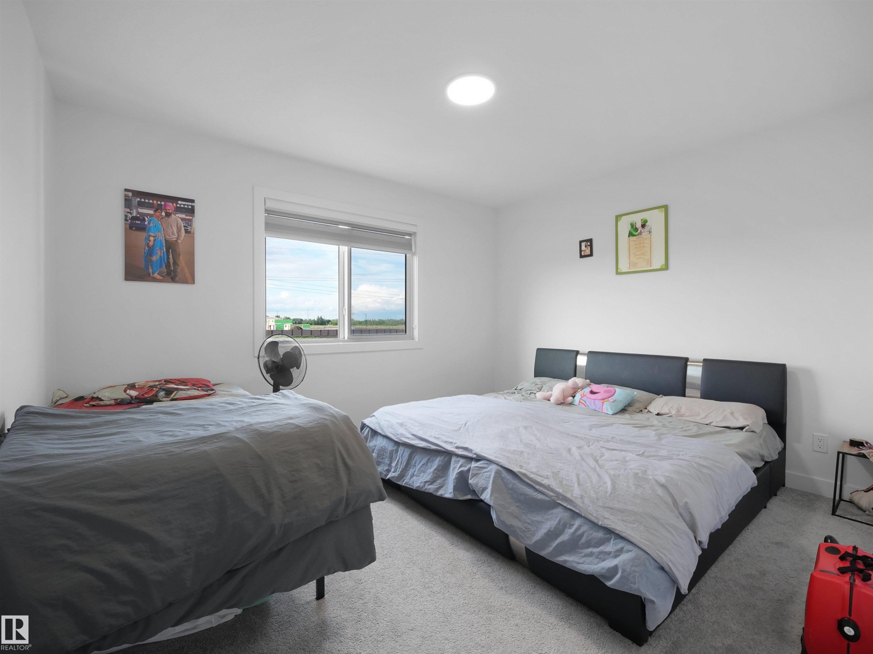 Bedroom featuring light gray carpeting, neutral white walls, a large window with white trim, and a ceiling-mounted light fixture - 19316 29 Avenue, Edmonton, AB