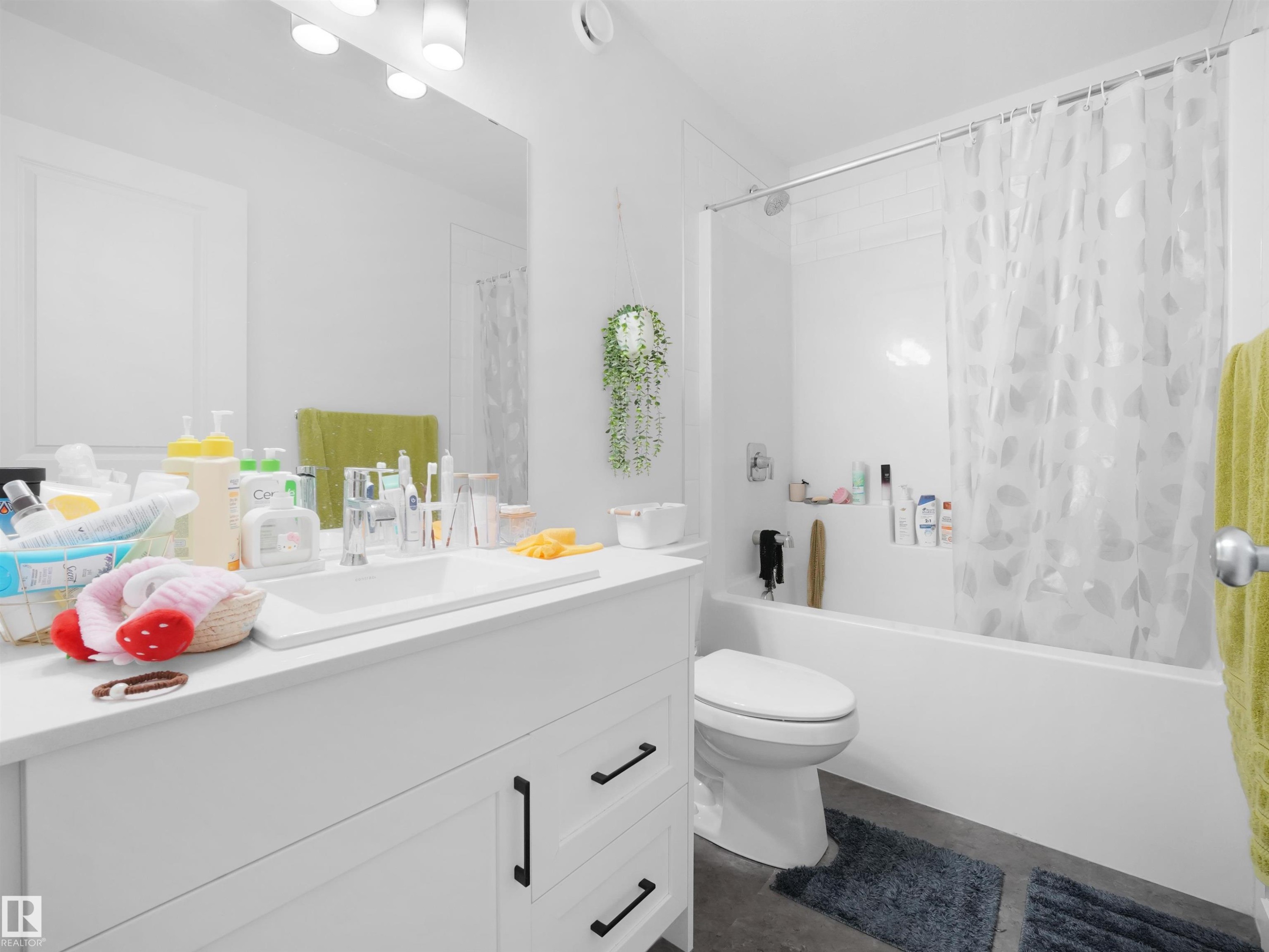 Bright bathroom featuring a white vanity with integrated sink, black hardware, a wide mirror, and a white bathtub with a shower kit - 19316 29 Avenue, Edmonton, AB