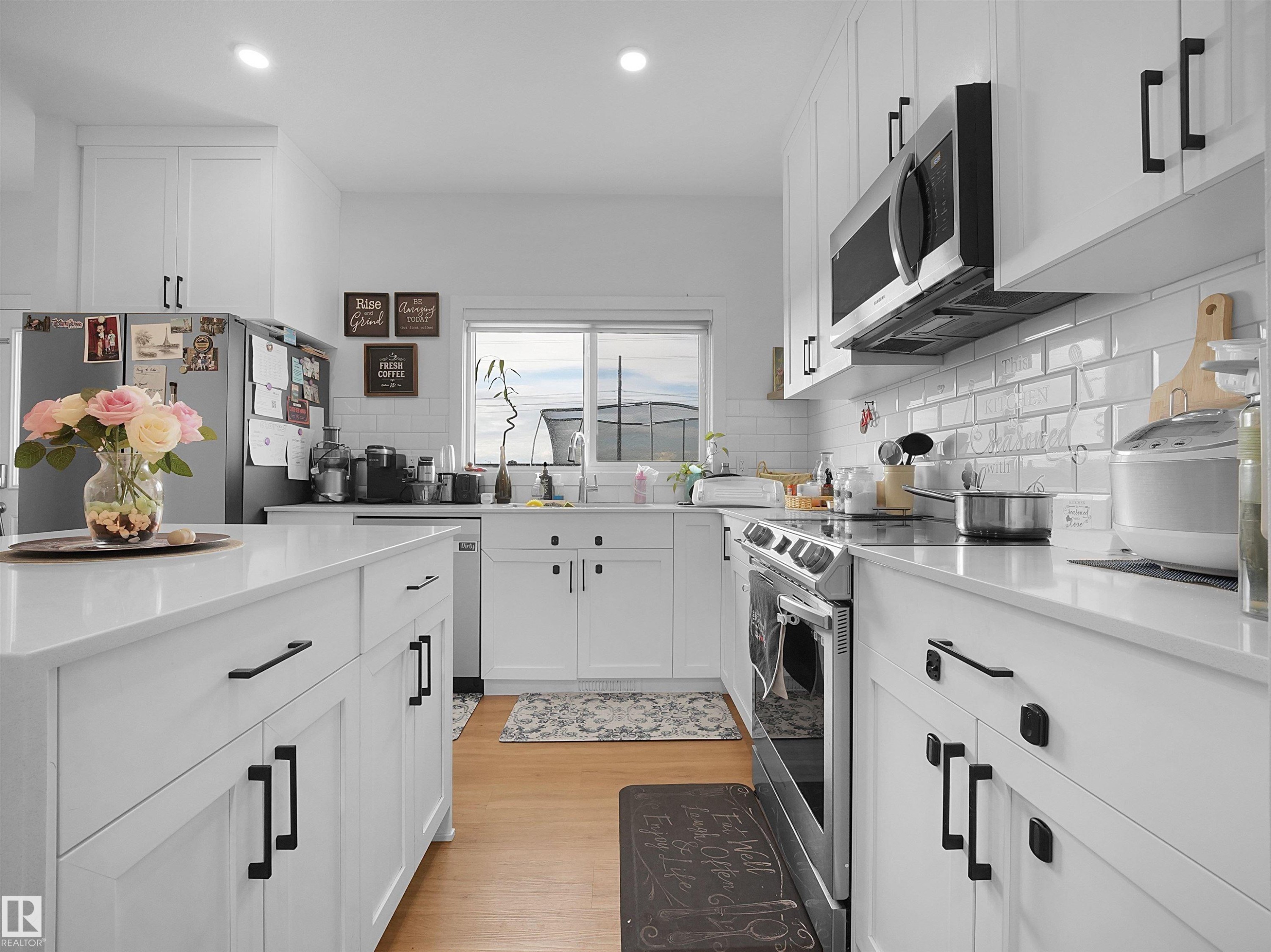 Bright kitchen featuring white cabinetry with black hardware, stainless steel appliances, a white subway tile backsplash, and light wood-finish flooring - 19316 29 Avenue, Edmonton, AB