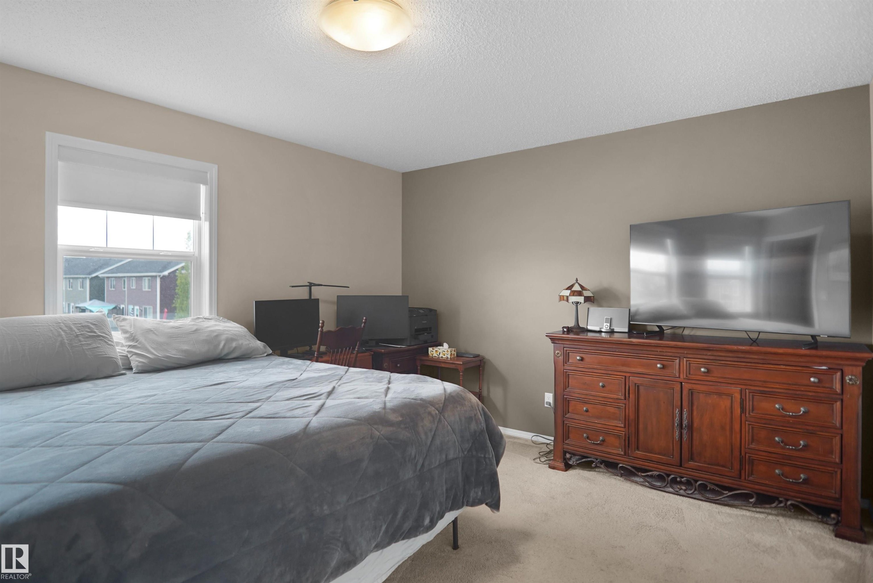 Carpeted bedroom featuring a large window with white trim, a flush-mount ceiling light fixture, and neutral-toned wall paint - 292 Simmonds Way, Leduc, AB