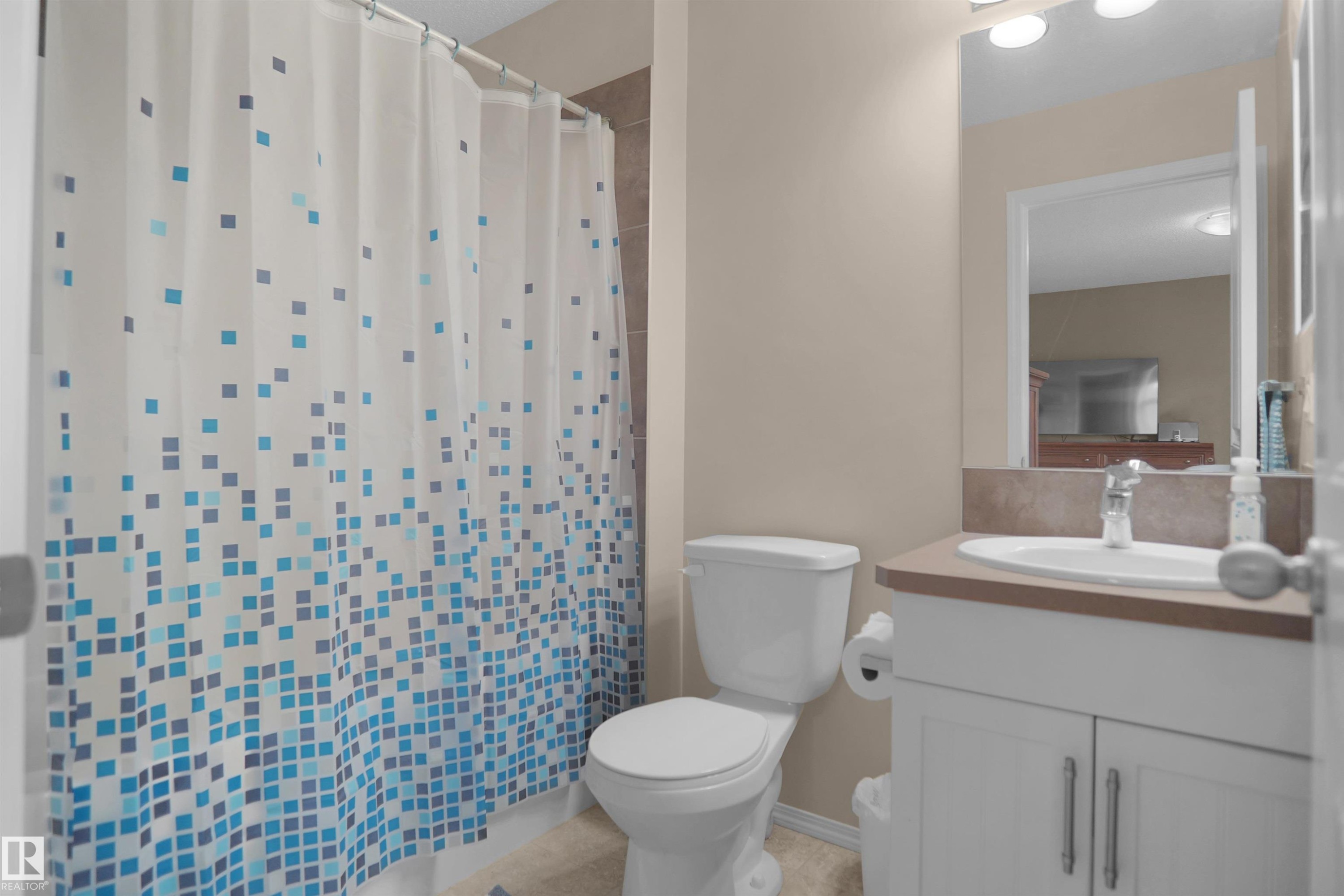 Bathroom featuring a white vanity with double-door cabinetry, an integrated sink, a neutral countertop, and a wall-mounted mirror with overhead lighting - 292 Simmonds Way, Leduc, AB
