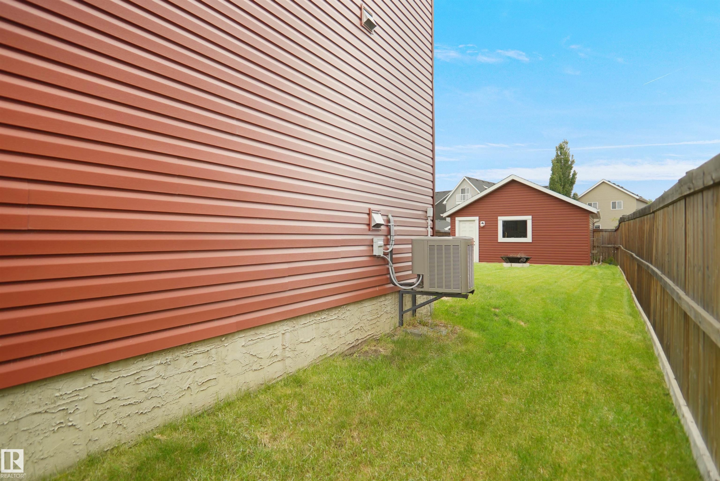 Expansive backyard featuring a manicured lawn, a detached red auxiliary building with a window and white trim, and a wooden privacy fence - 292 Simmonds Way, Leduc, AB
