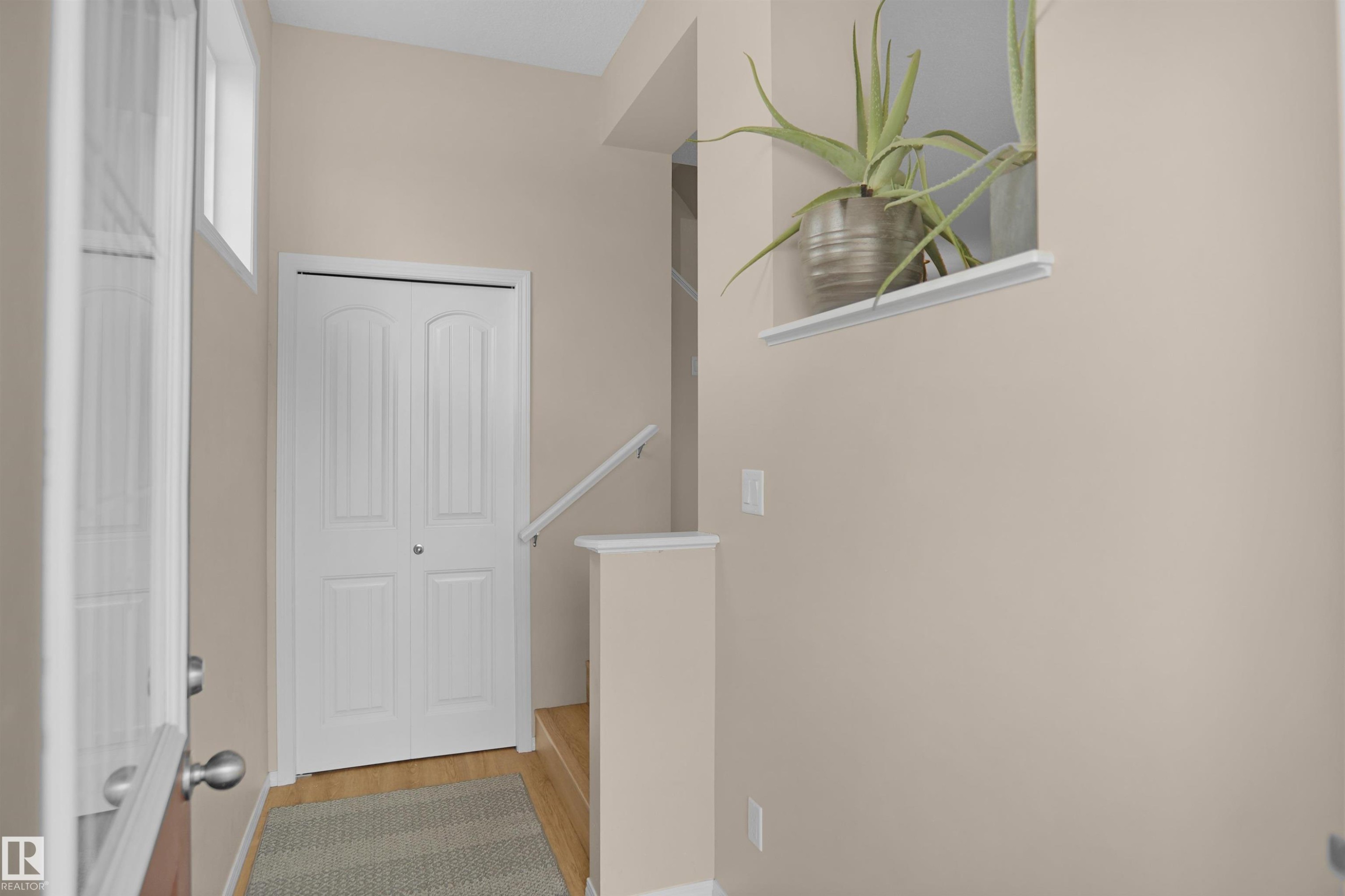 Entryway featuring a white bi-fold door, wood-finish flooring, and a window providing natural illumination - 292 Simmonds Way, Leduc, AB