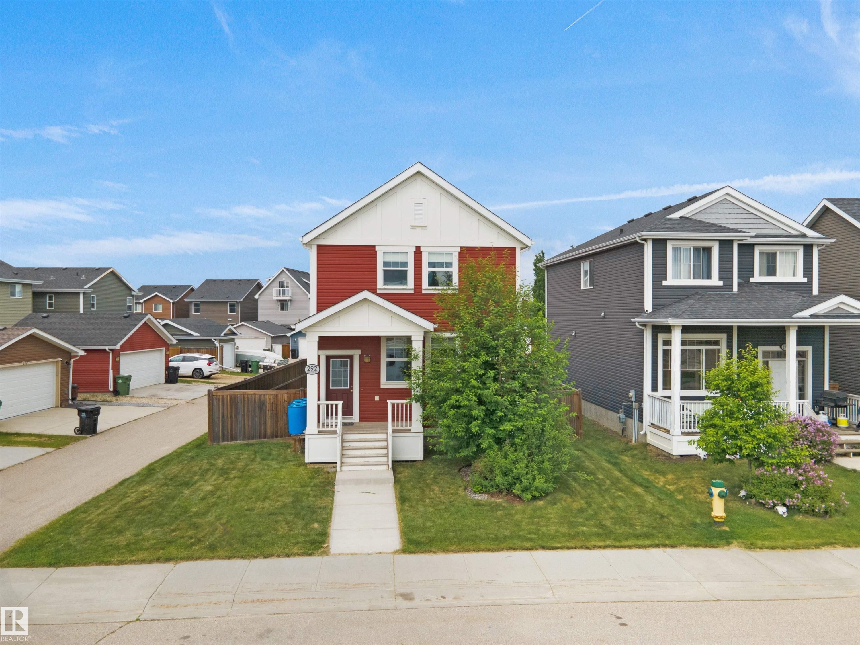 Two-story residence featuring red siding with white trim and a covered front porch - 292 Simmonds Way, Leduc, AB