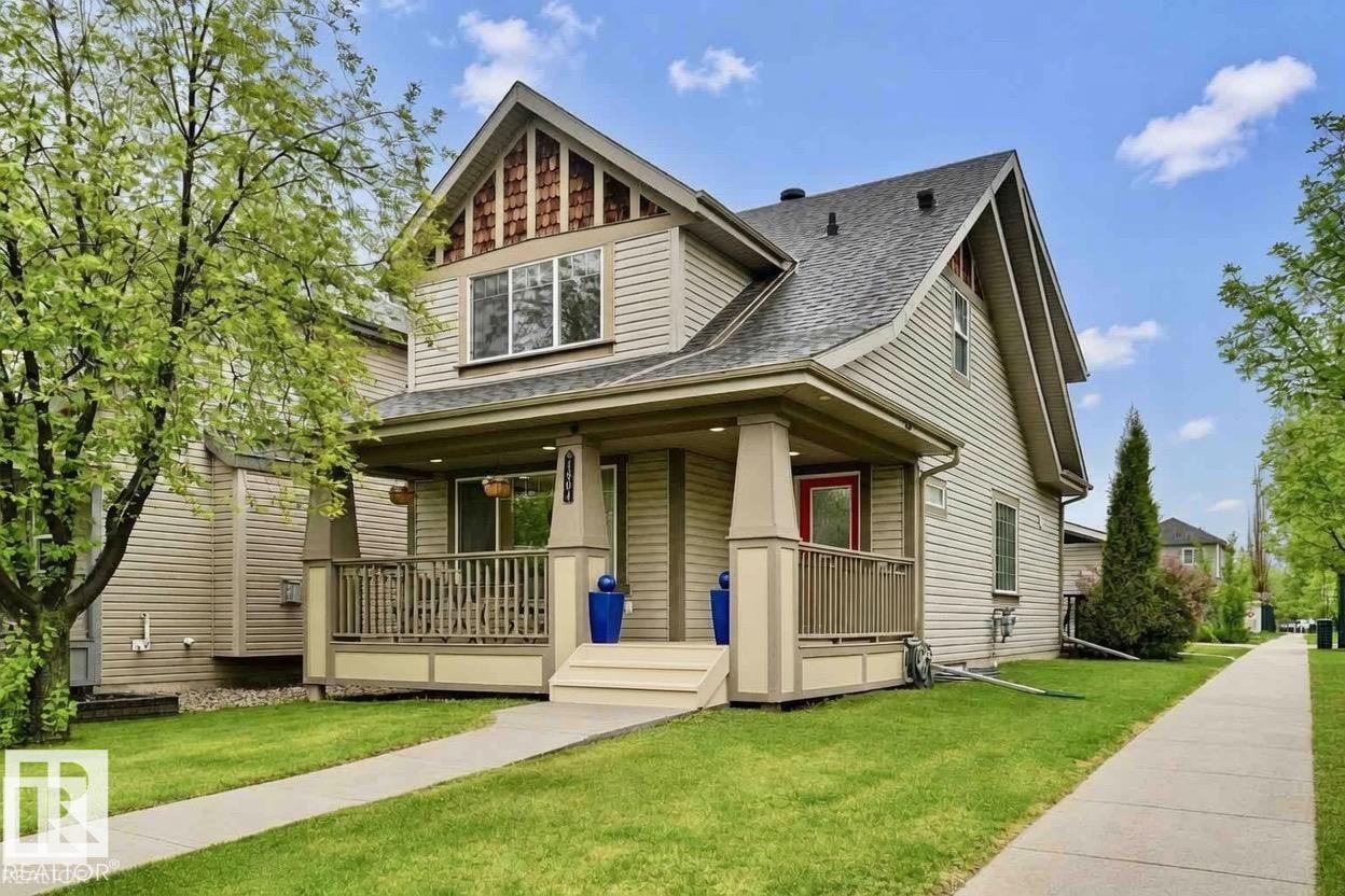 Two-story residence featuring light beige siding, a dark shingled roof, a covered front porch with railing, a red entry door, and a concrete front walkway - 1804 121 Street, Edmonton, AB