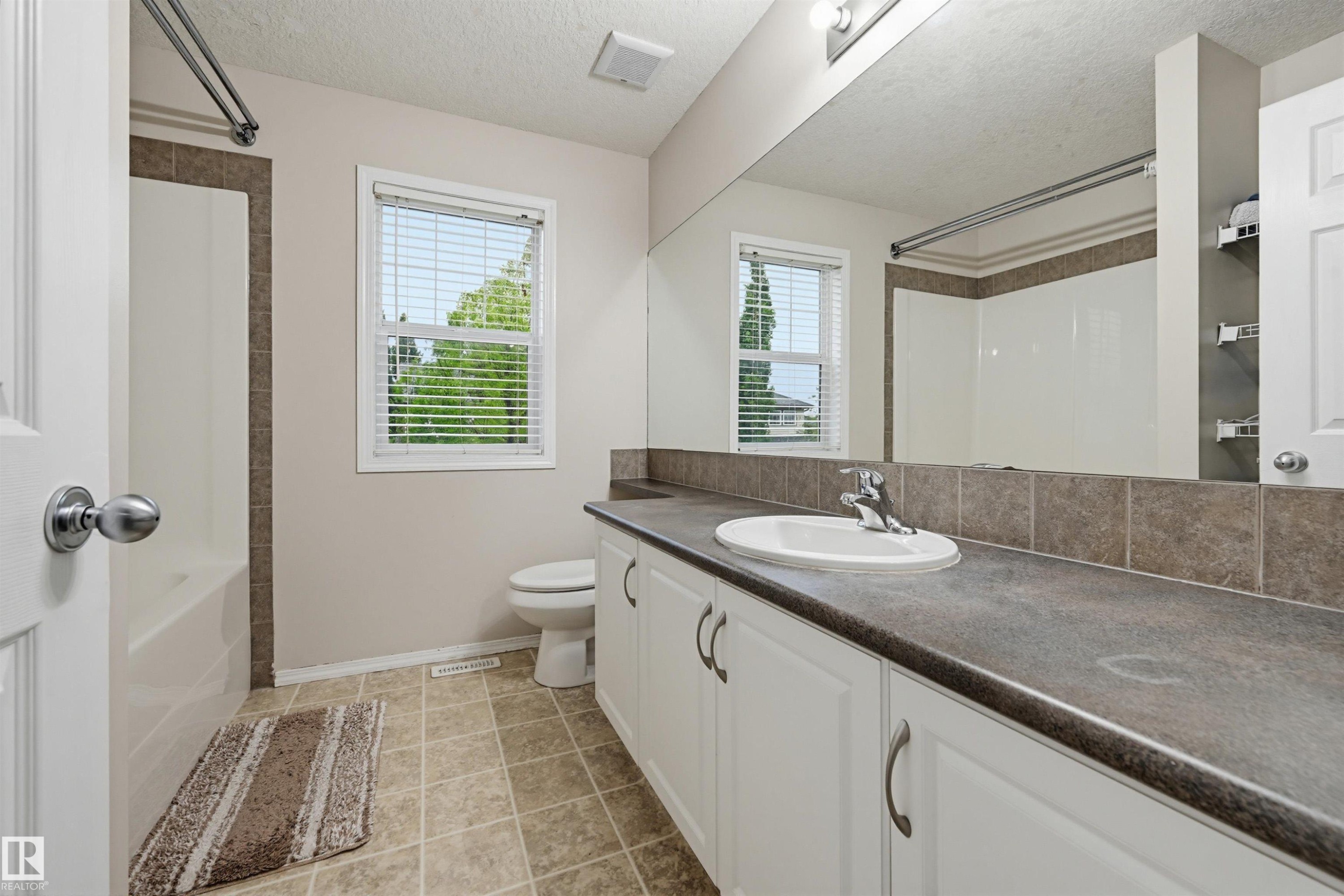 Bathroom featuring a spacious vanity with an integrated sink, ample counter space, white cabinetry, and a full-width mirror - 1804 121 Street, Edmonton, AB
