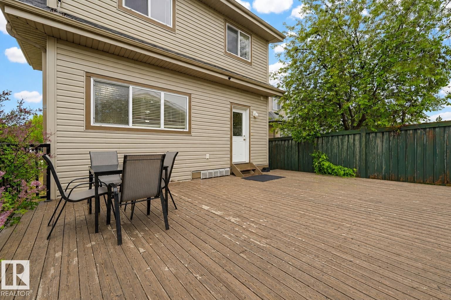 Expansive wood-finish deck with direct exterior access, featuring horizontal siding, multiple windows, and a surrounding privacy fence - 1804 121 Street, Edmonton, AB