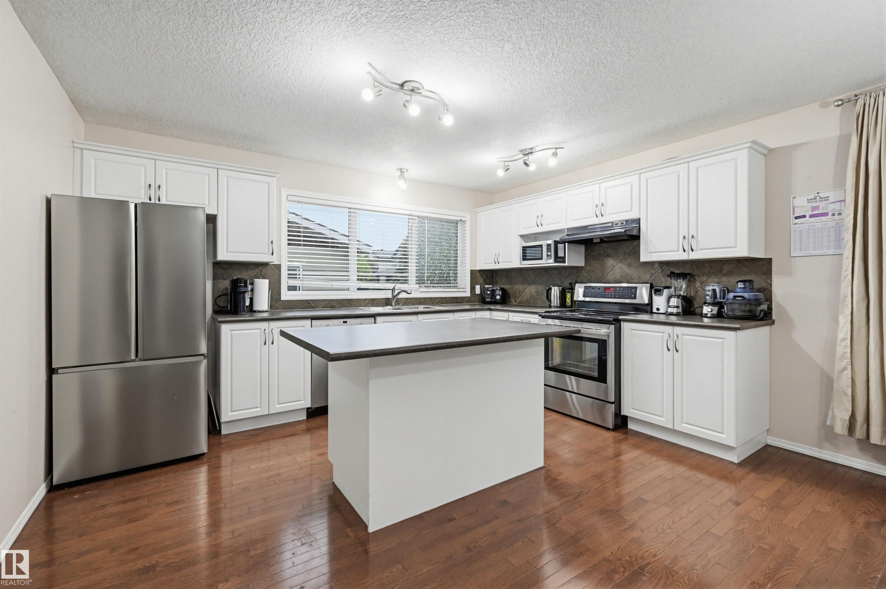 Kitchen featuring dark wood-finish flooring, white cabinetry, stainless steel appliances, and a central island with a dark countertop - 1804 121 Street, Edmonton, AB