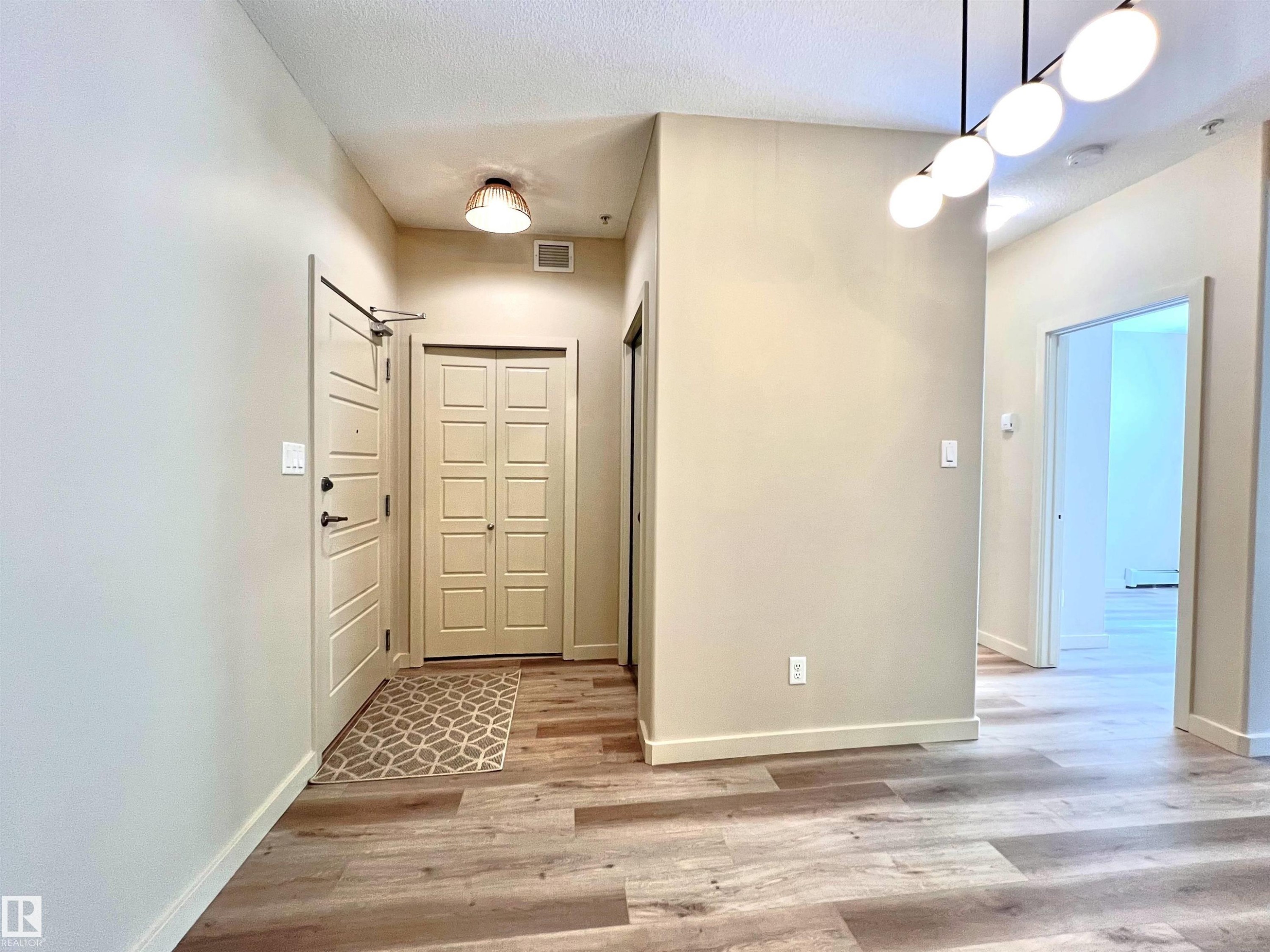 Entryway featuring wood-finish flooring, a contemporary linear chandelier, recessed lighting, and a paneled entry door - 140 308 Ambleside Link Link, Edmonton, AB