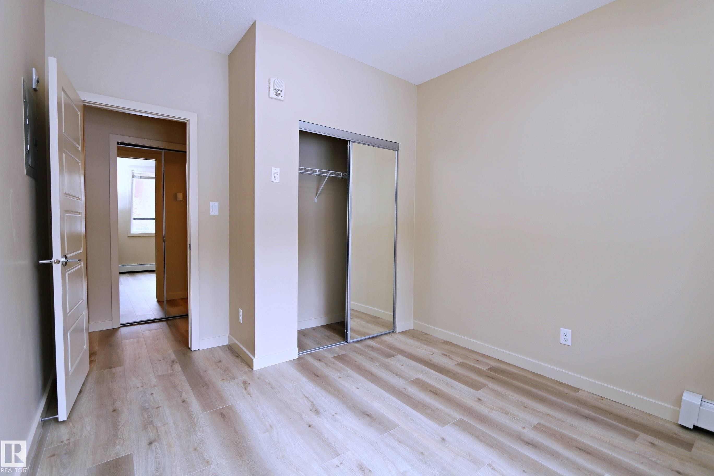 Bedroom featuring wood-finish flooring, neutral wall paint, and a mirrored sliding closet door - 140 308 Ambleside Link Link, Edmonton, AB