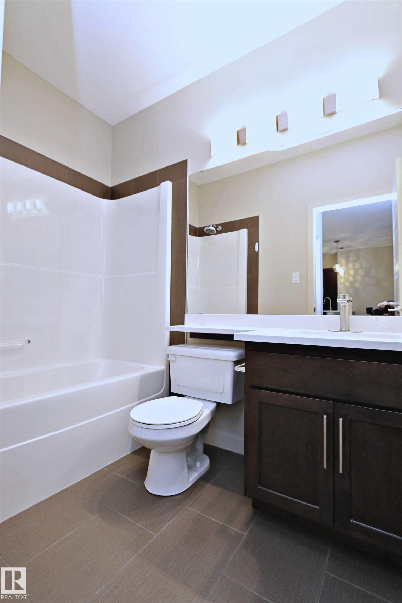 Bathroom featuring a white bathtub with a shower, a dark wood-finish vanity with a light countertop, and tile flooring - 140 308 Ambleside Link Link, Edmonton, AB