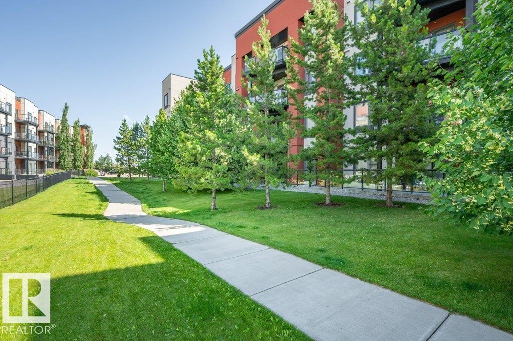 Landscaped grounds featuring a winding concrete pathway, mature evergreen trees, and a vibrant green lawn - 140 308 Ambleside Link Link, Edmonton, AB