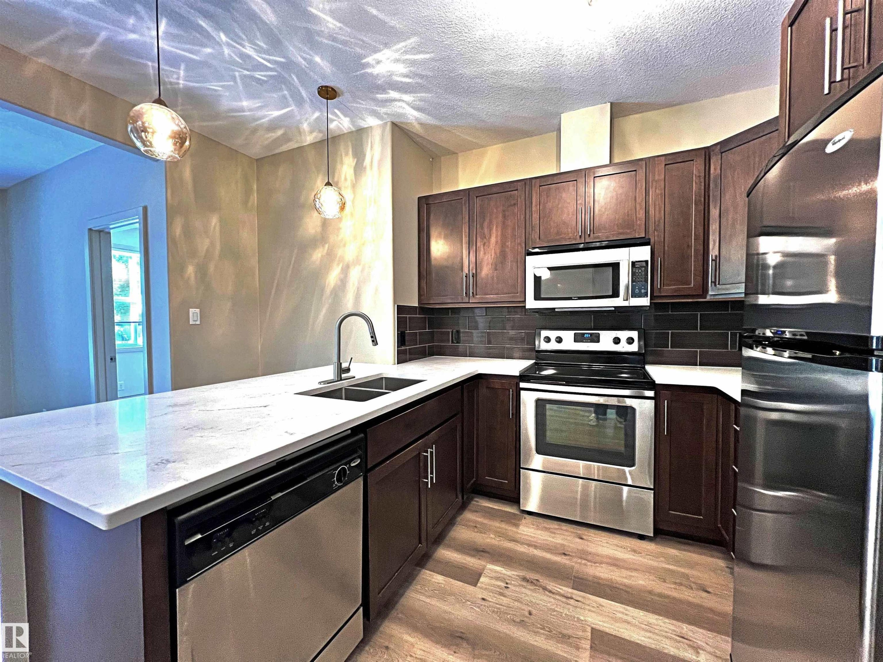 Modern kitchen featuring wood-finish flooring, dark wood cabinetry, white countertops, and a subway tile backsplash - 140 308 Ambleside Link Link, Edmonton, AB