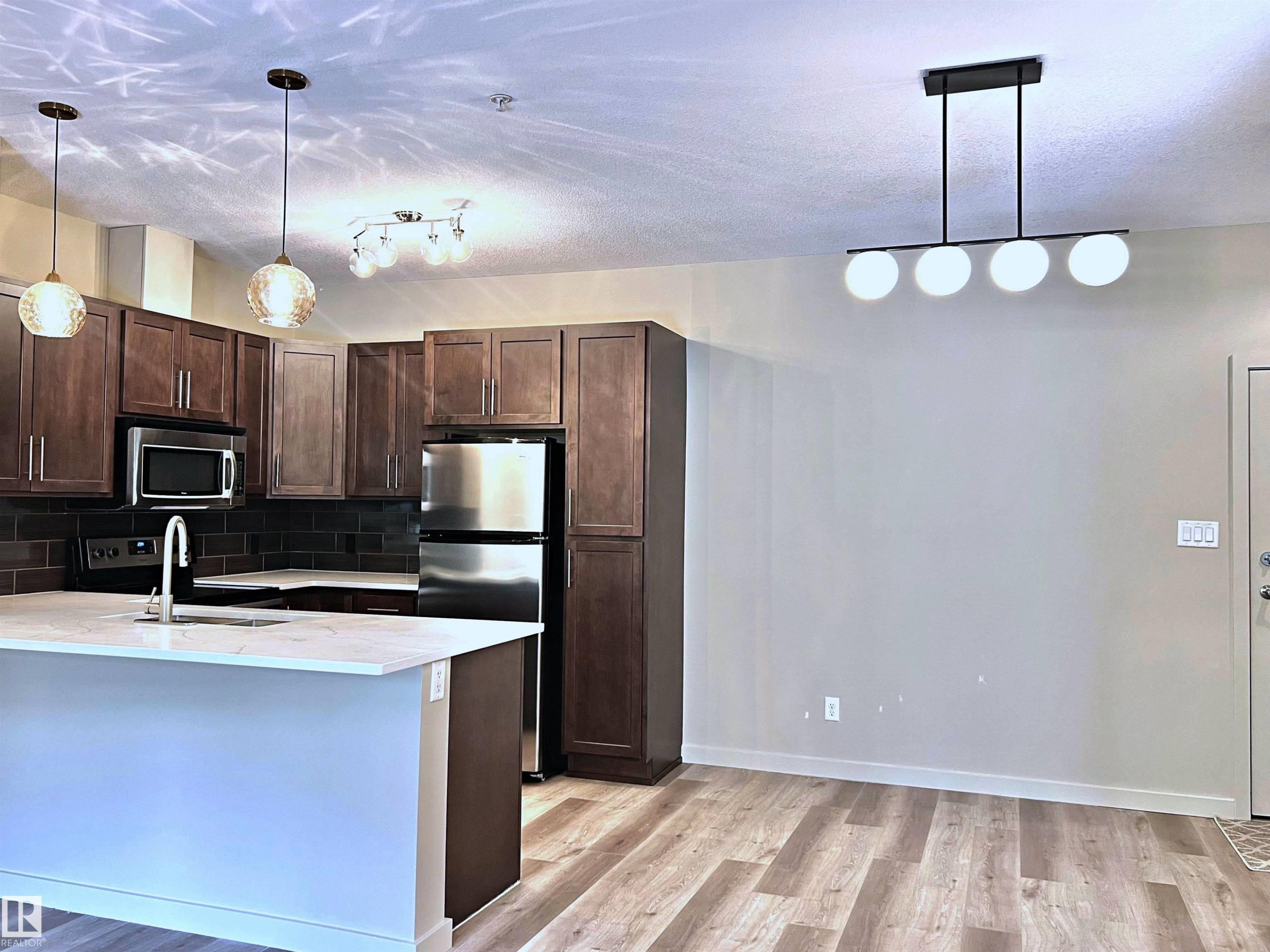 Modern kitchen featuring wood-finish flooring, stainless steel appliances, dark wood cabinetry, white countertops, and a dark subway tile backsplash - 140 308 Ambleside Link Link, Edmonton, AB