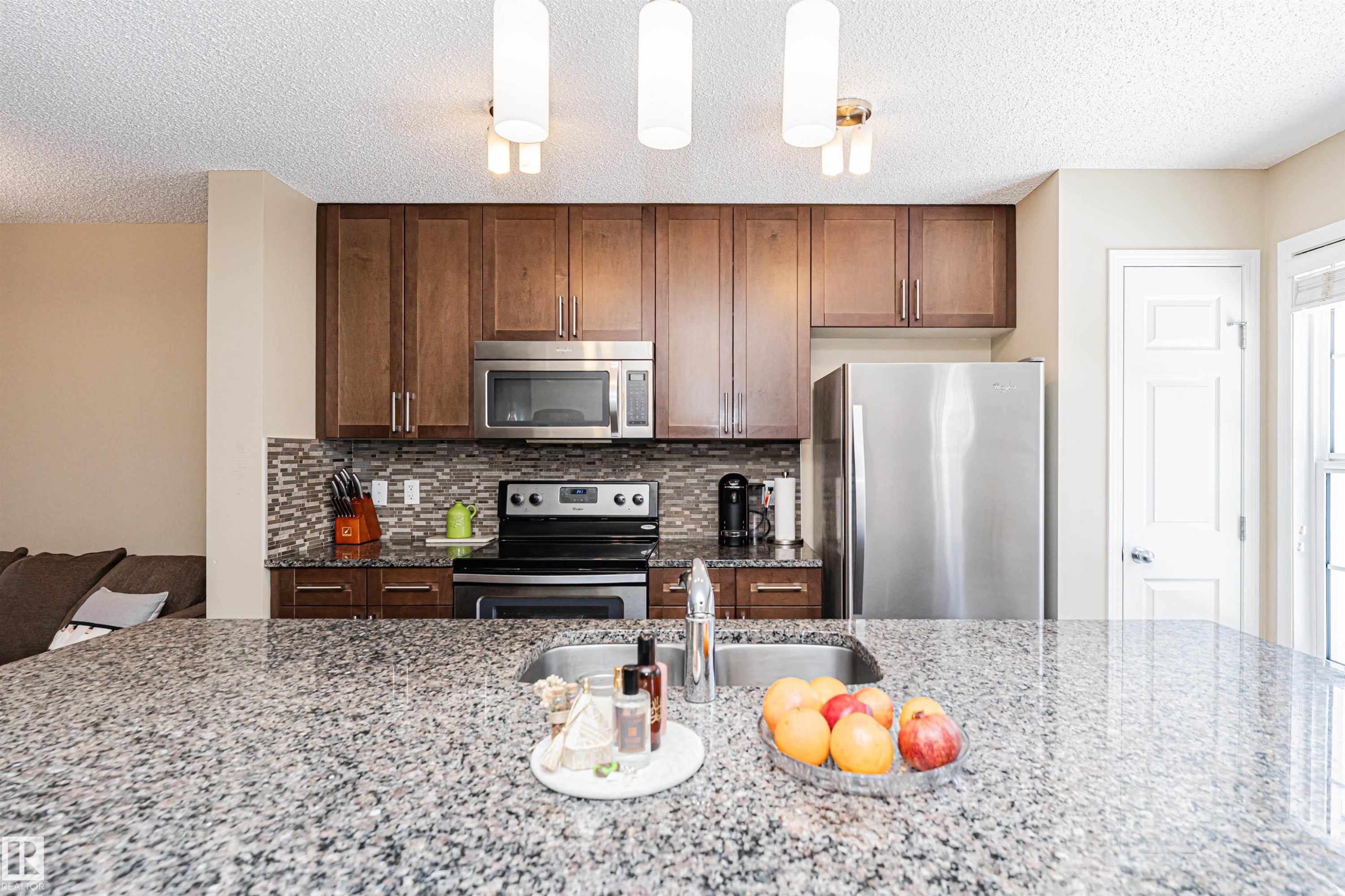 Kitchen featuring granite countertops, wood cabinetry, stainless steel appliances, and a mosaic tile backsplash - 31 4029 Orchards Drive, Edmonton, AB