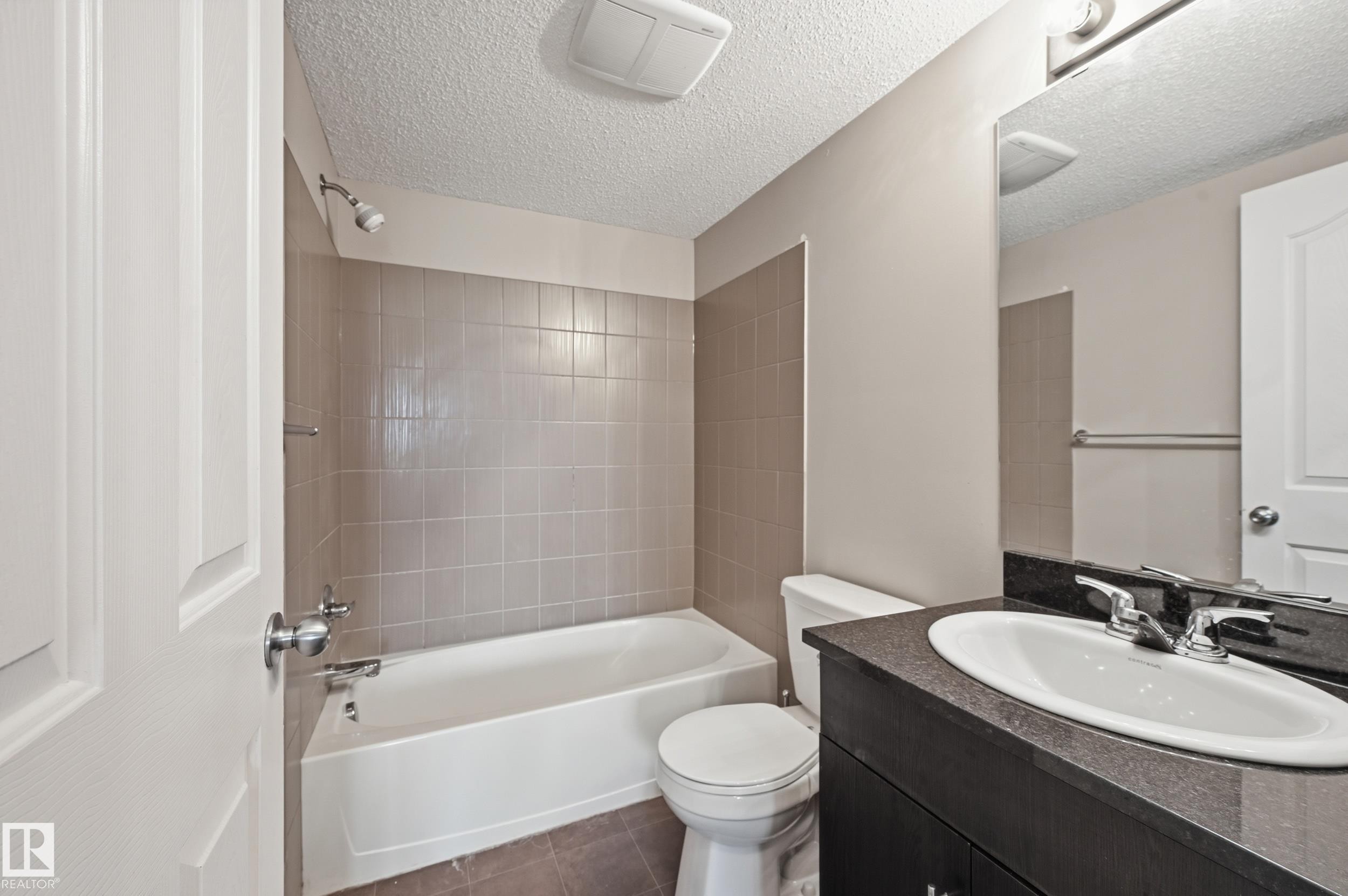 Bathroom featuring a white bathtub, tiled shower surround, dark vanity with an integrated sink, and a wall-mounted mirror - 304 11804 22 Avenue, Edmonton, AB