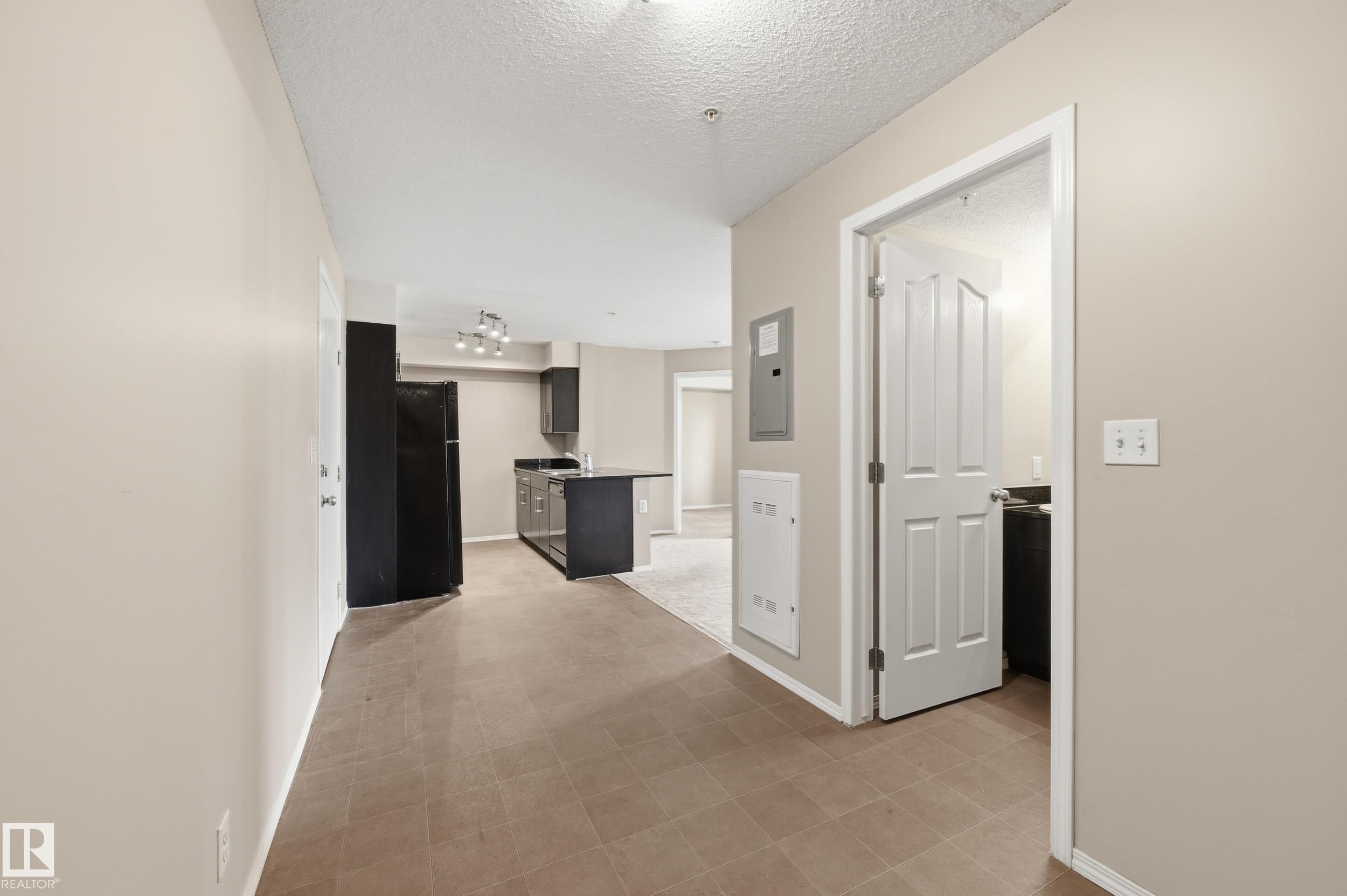 Open-concept living space featuring ceramic tile flooring, a black refrigerator, dark cabinetry, and a track lighting fixture - 304 11804 22 Avenue, Edmonton, AB